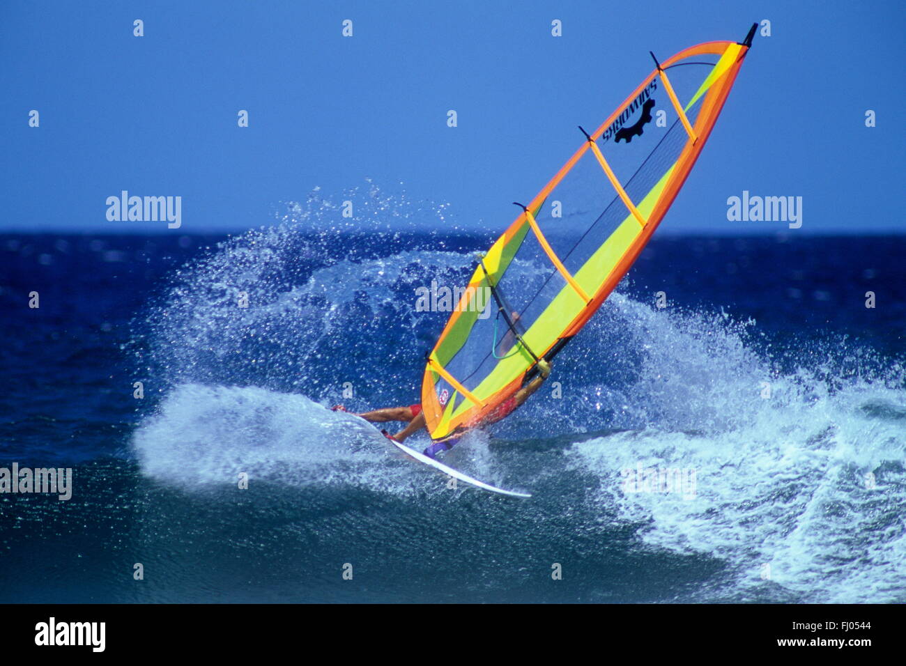 Fast skating über die Welle ein Windsurfer führt mit leuchtend gelbes Segel am Pazifischen Meer am Hookipa, Hawaii, USA Stockfoto