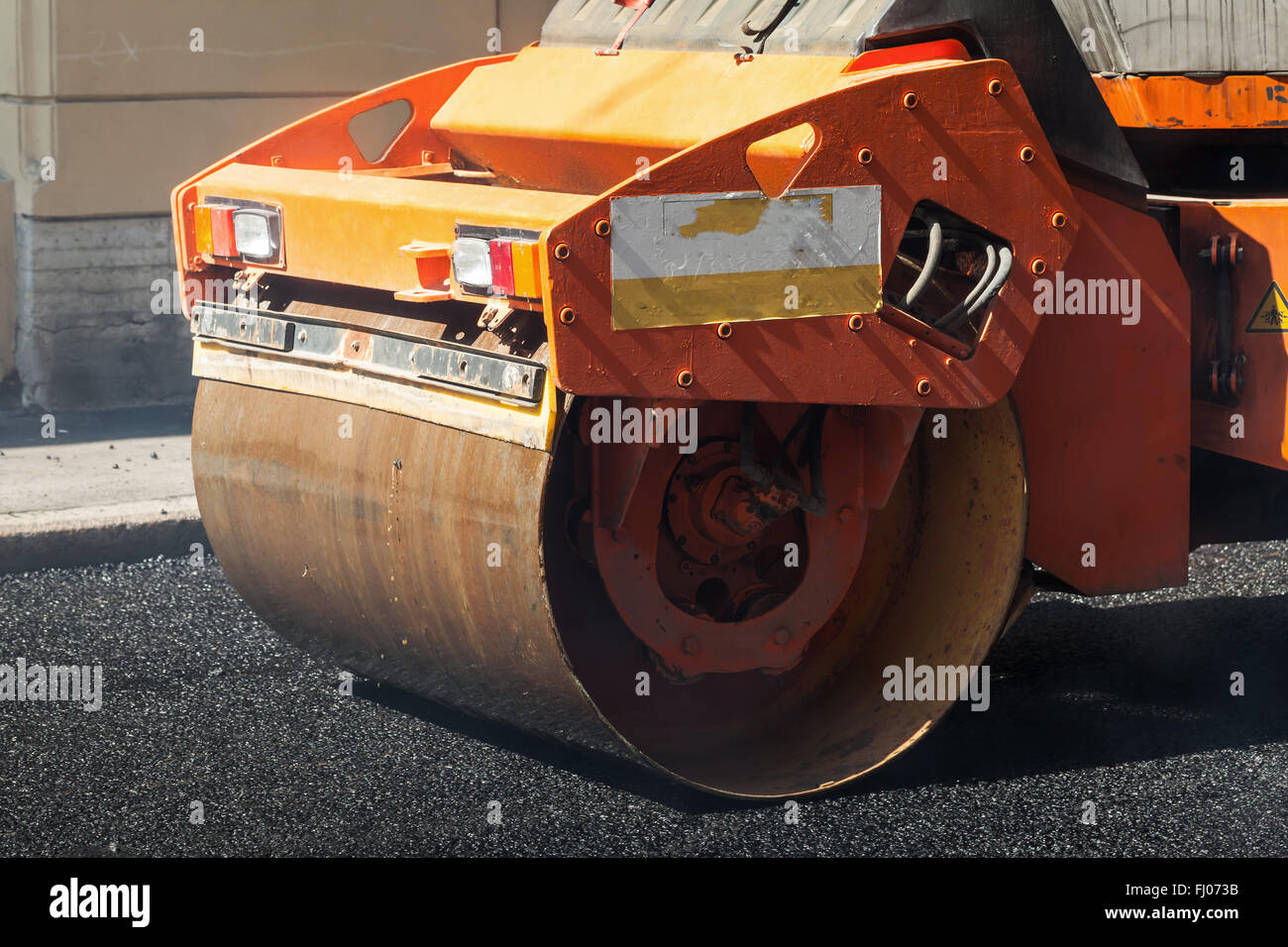 Fragment der orange Walze, städtische Straße befindet sich im Aufbau, Asphaltierung im Gange Stockfoto