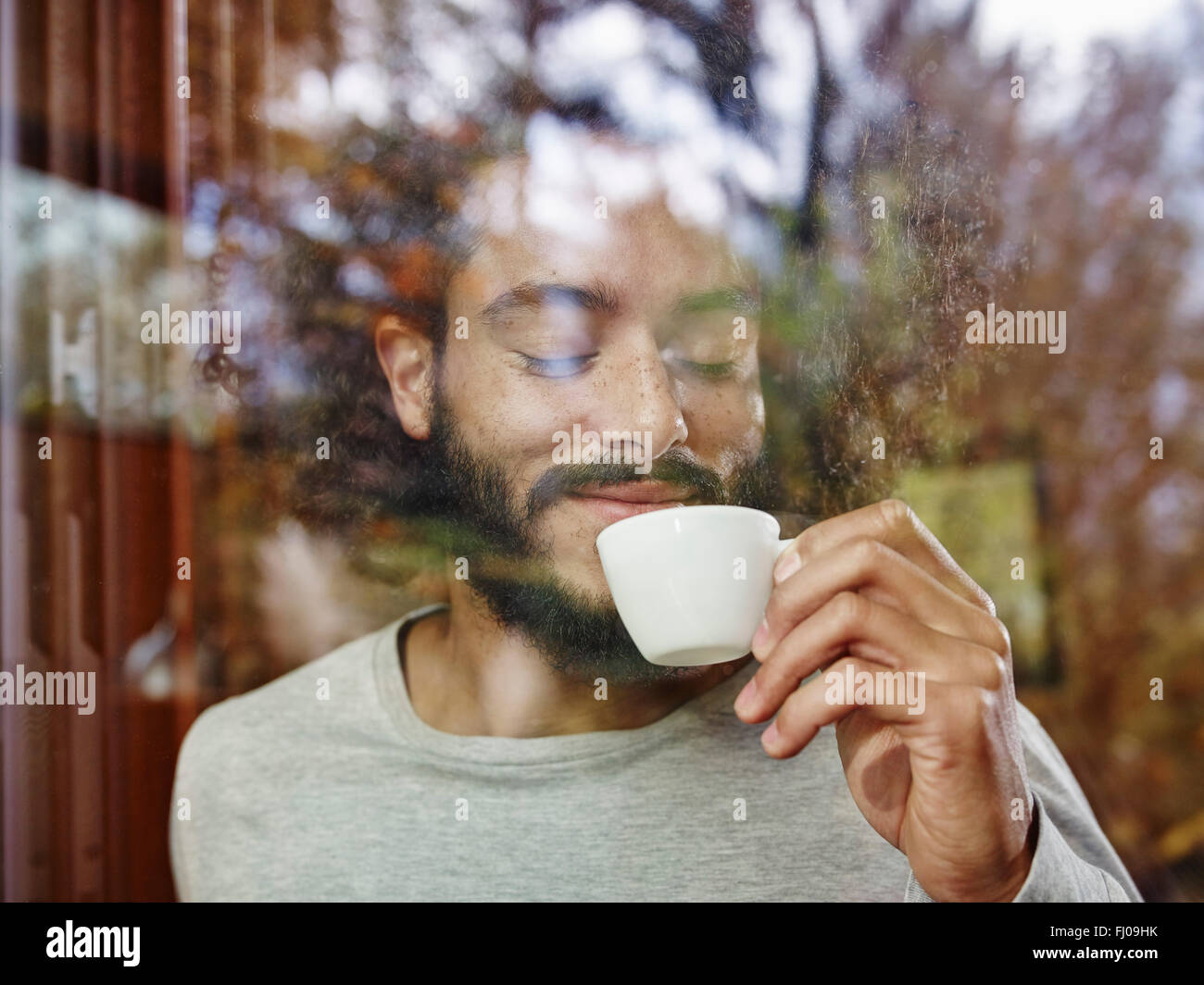 Lächelnd jungen Mann Tasse Kaffee hinter Fensterscheibe Stockfoto