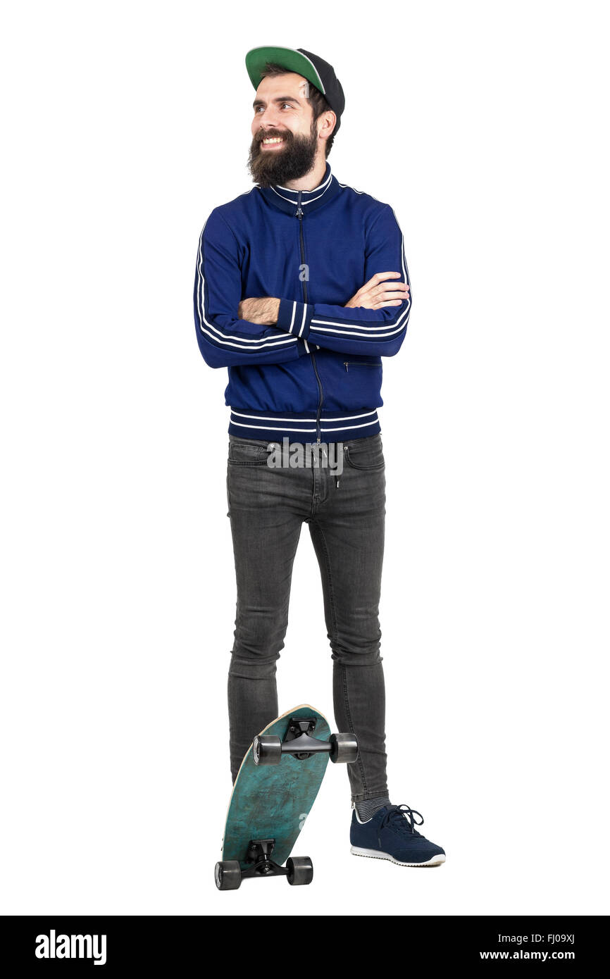 Junge Hipster in blauem Trainingsanzug Jacke und Mütze auf Skateboard suchen Sie lächelnd. Ganzkörper-Länge-Porträt isoliert auf weiss Stockfoto