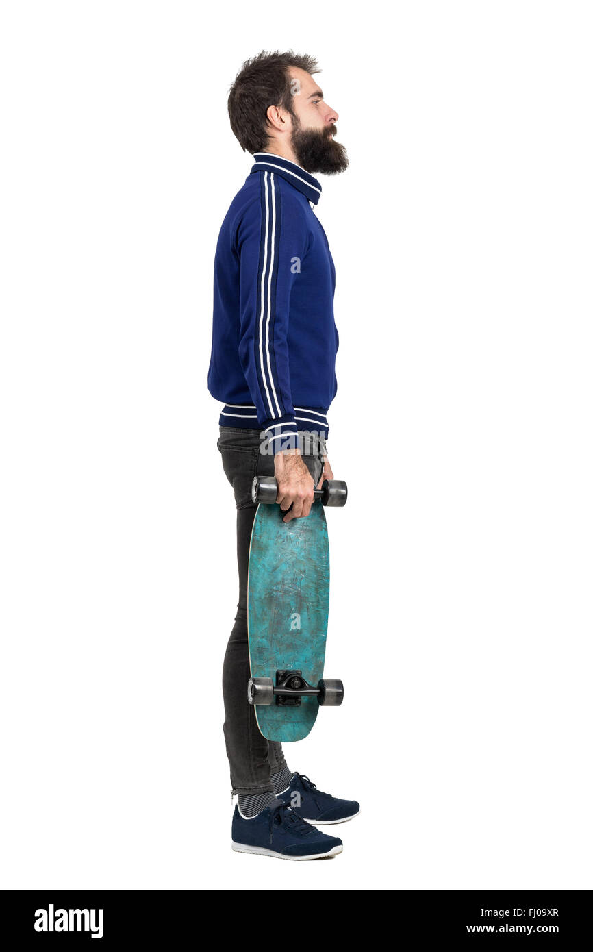 Seitenansicht der junge bärtige Hipster im Trainingsanzug Jacke tragen Skateboard. Ganzkörper-Länge-Porträt über weißen isoliert Stockfoto