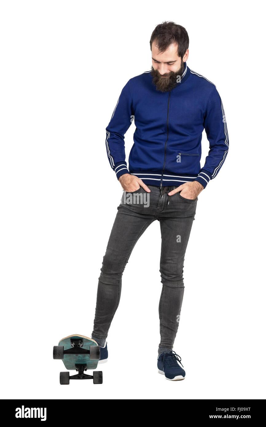 Lächelt zuversichtlich Hipster tragen blaue Trainingsanzug und engen Jeans auf Skateboard. Ganzkörper-Länge-Porträt isoliert auf weiss Stockfoto