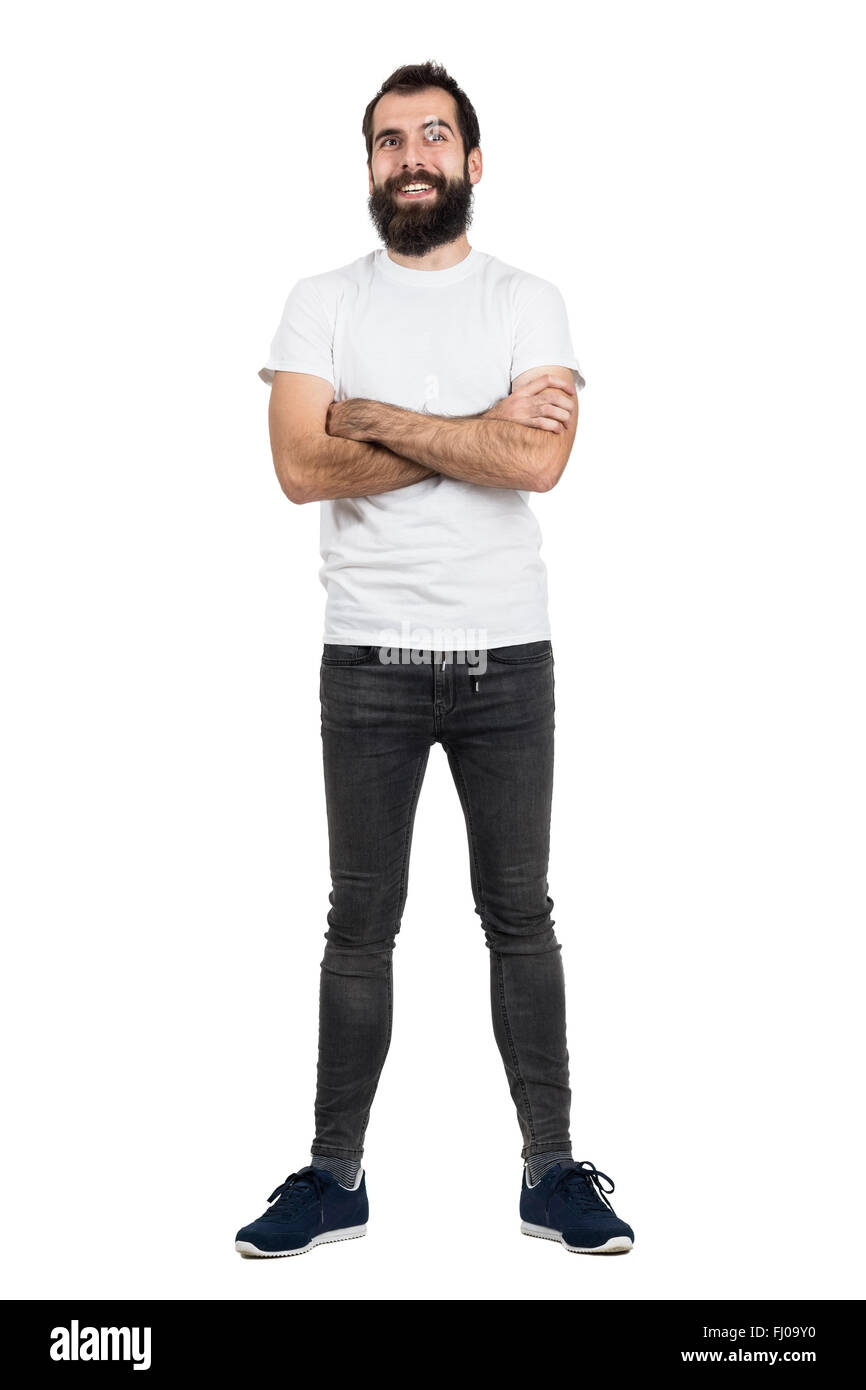 Glücklich positive bärtige Hipster in weißem T-shirt und enge Jeans mit verschränkten Armen. Ganzkörper-Länge-Porträt über weißen isoliert Stockfoto