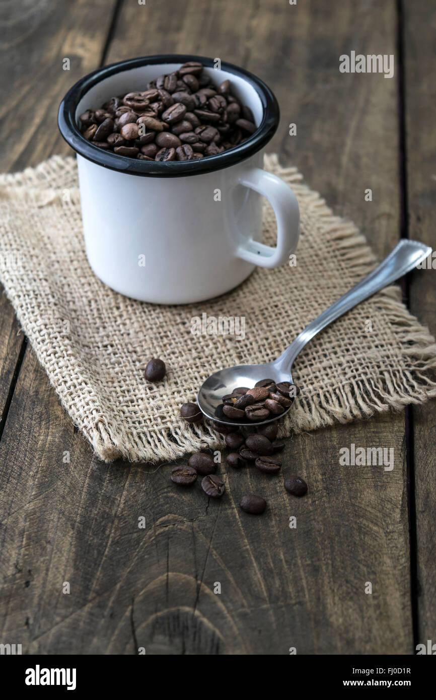 Kaffeebohnen in ein Emaille Becher auf dem hölzernen Hintergrund Stockfoto
