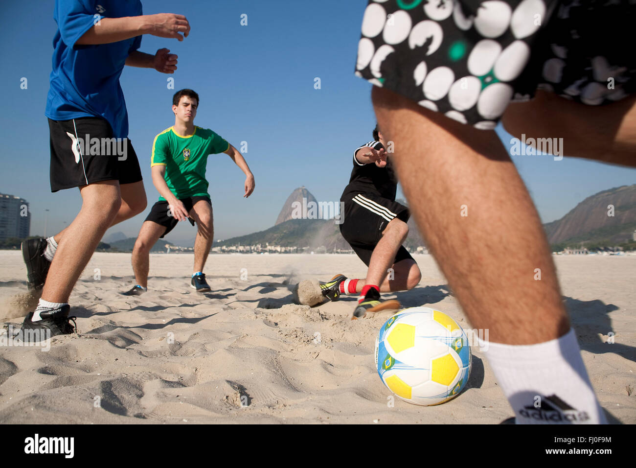 Junge Männer spielen Fußball am Strand von Botafogo in Rio De Janeiro, Brasilien - Zuckerhut im Hintergrund. Stockfoto