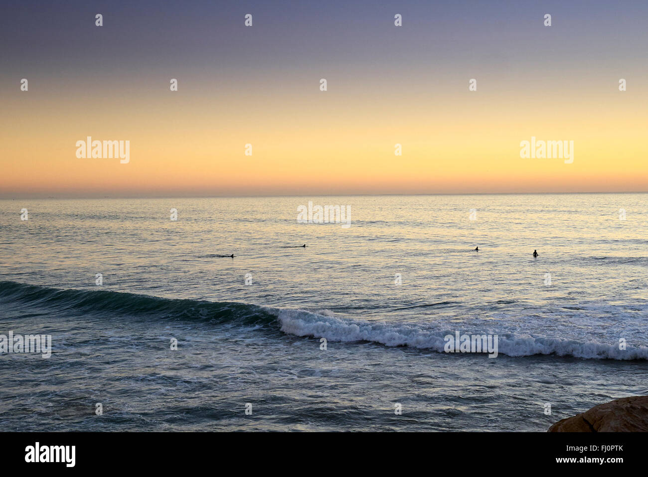 Blick auf den Sonnenuntergang von dem kleinen Fischerdorf Taghazout - Marokko. Surfer, die darauf warten, den letzten der Wellen zu fangen. Stockfoto