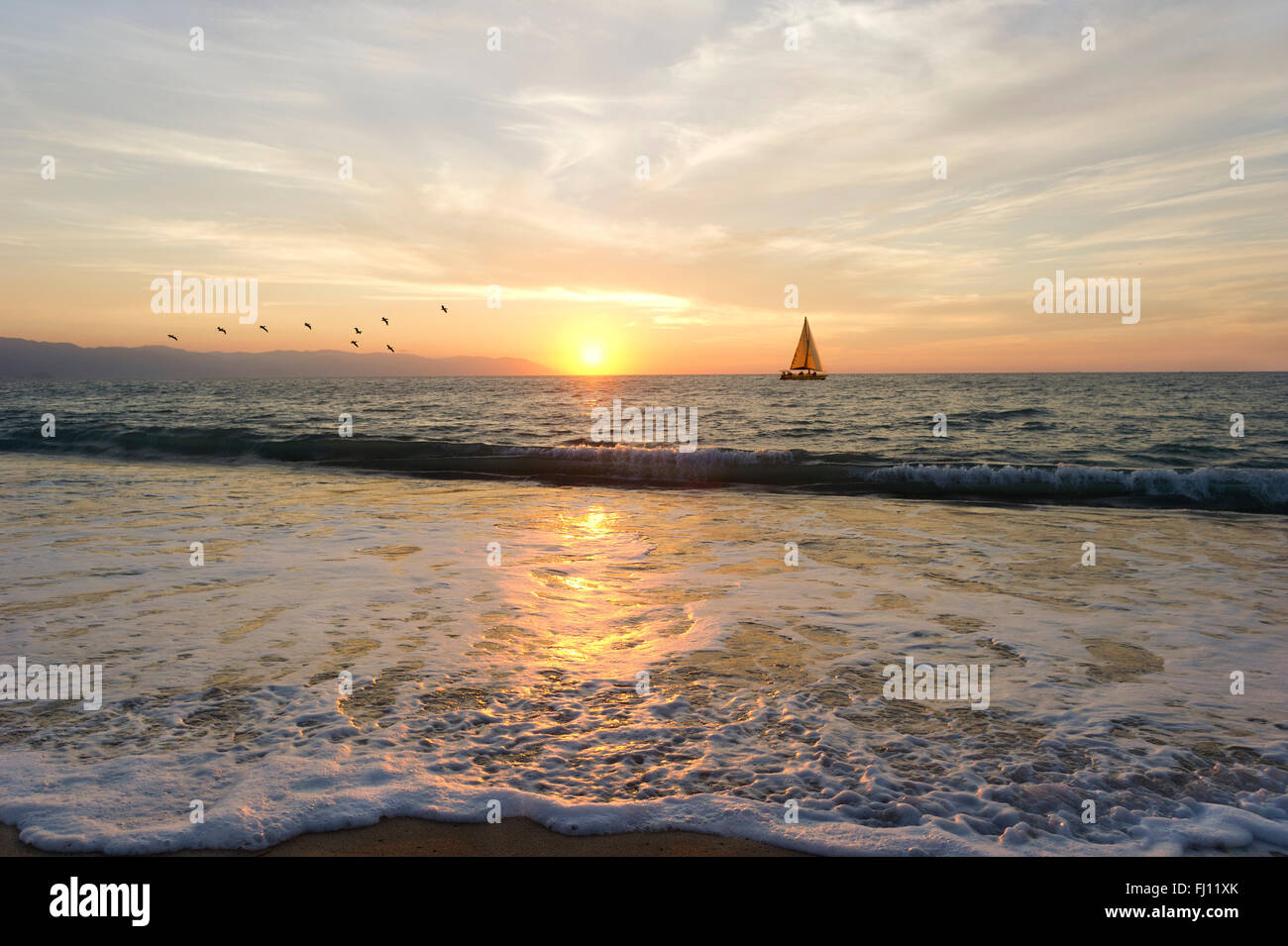 Segelboot Sonnenuntergang ist ein Segelboot mit Menschen an Bord nahe der Küste mit einer sanften Welle rollt und den Sonnenuntergang am Meer. Stockfoto