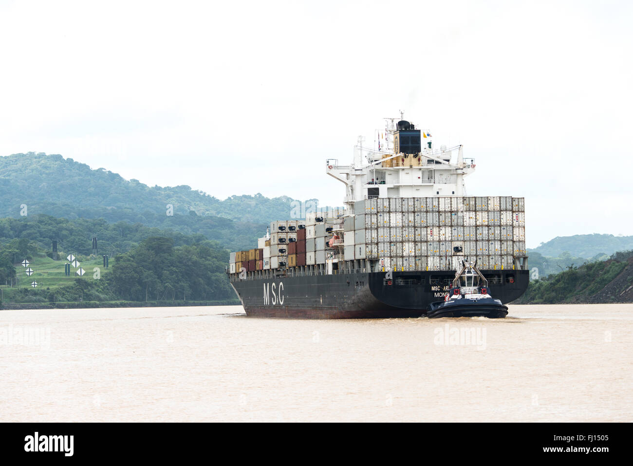 Panamakanal, Panama--ein Schlepper hilft ein großes Containerschiff eine Engstelle des Panama-Kanals zu navigieren. Im Jahr 1914 eröffnet, ist der Panamakanal eine entscheidende Schifffahrtsweg zwischen der Atlantischen und Pazifischen Ozean, das bedeutet, dass Schiffe nicht haben, um den Boden in Südamerika oder über der Oberseite von Kanada zu gehen. Der Kanal wurde ursprünglich gebaut und im Besitz von den Vereinigten Staaten, aber wurde im Jahr 1999 zurück nach Panama übergeben. Stockfoto