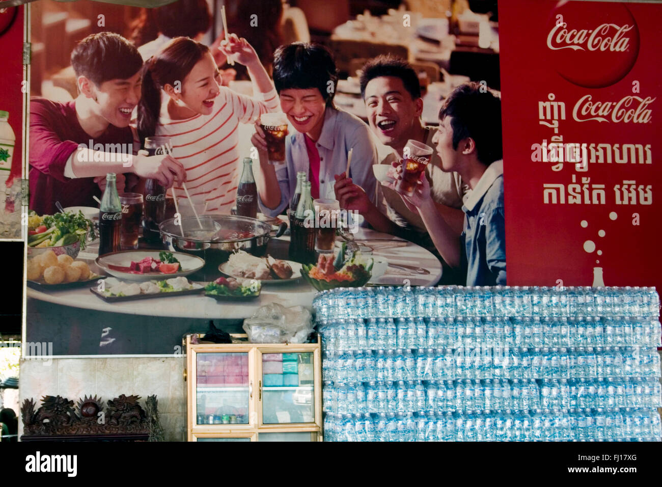Kunststoff-Flaschen sind unter einem großen Coca Cola Werbung Schild in einem Restaurant in Skun, Provinz Kampong Cham, Kambodscha gestapelt. Stockfoto