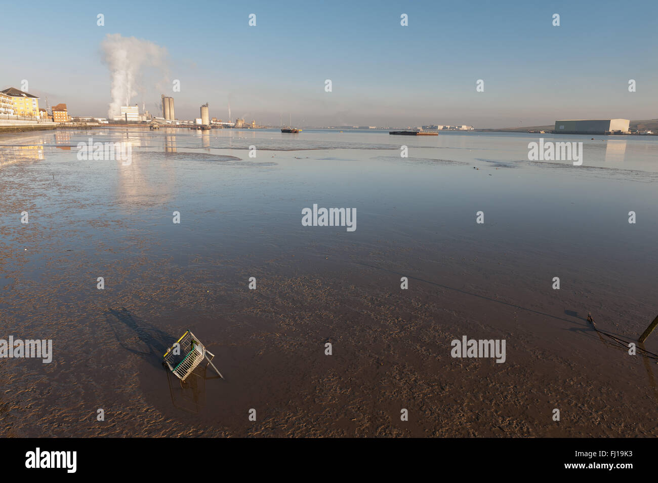 Einkaufswagen in Versenkung Schlamm in Thames Becken am Erith mit umweltschädliche Fabriken im Hintergrund verworfen Stockfoto