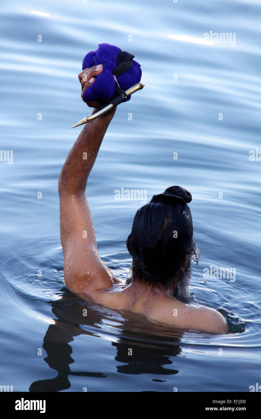 Ein Mann nimmt ein Bad im heiligen Wasser um die Goldenen Tempel und hob seinen Kirpan in der Luft, Amritsar, Indien Stockfoto