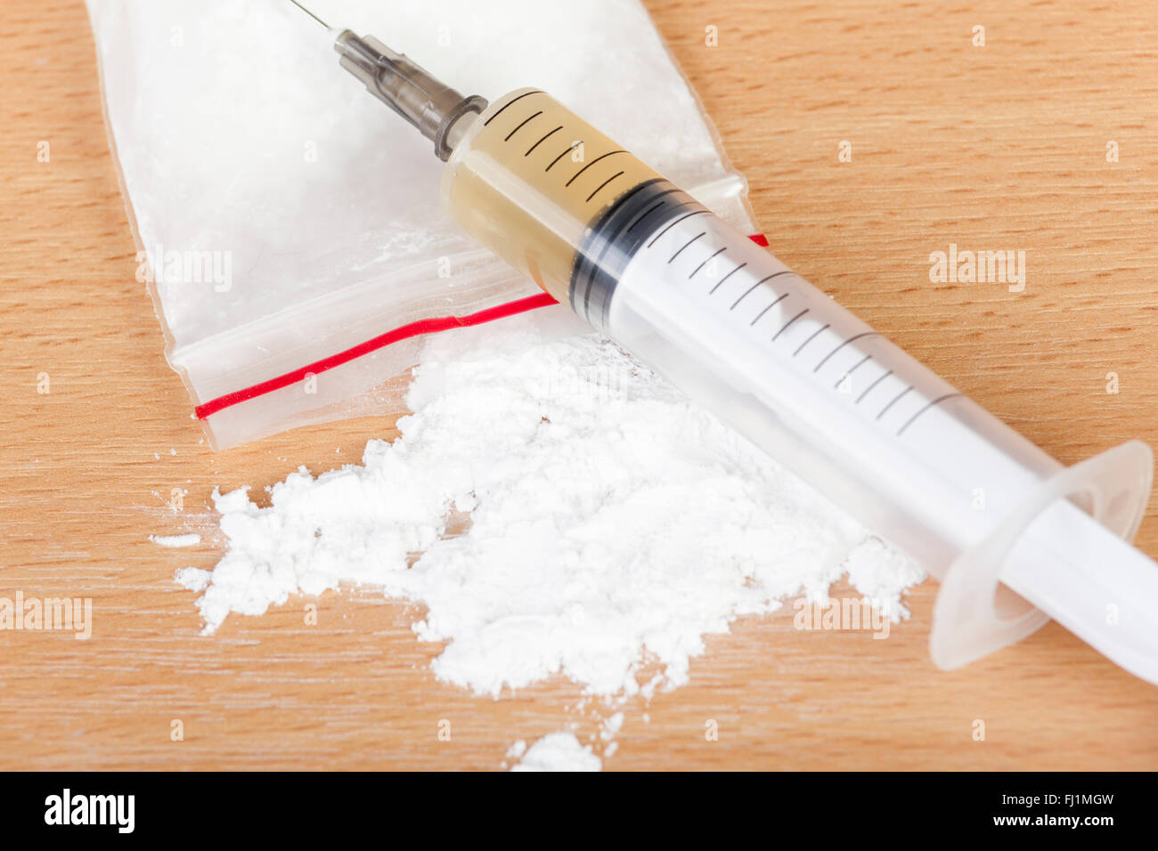 Geladen Heroin Spritze über eine verschüttete Tasche von Heroin auf einen Tisch legen Stockfoto