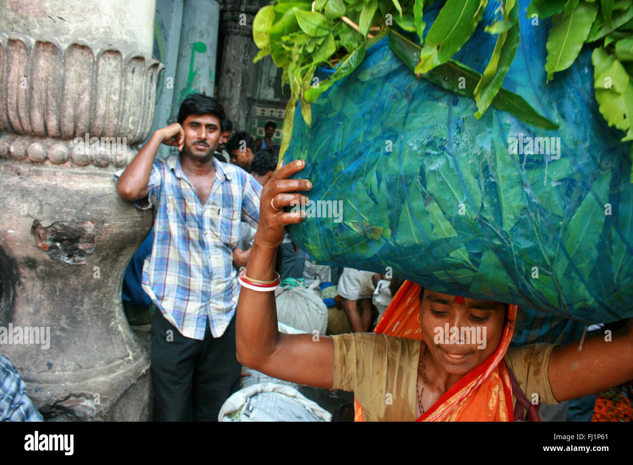Frau, die schwere Tasche - harte Arbeit bei Kalkutta Blumenmarkt, Indien. Ein Mann wacht. Stockfoto
