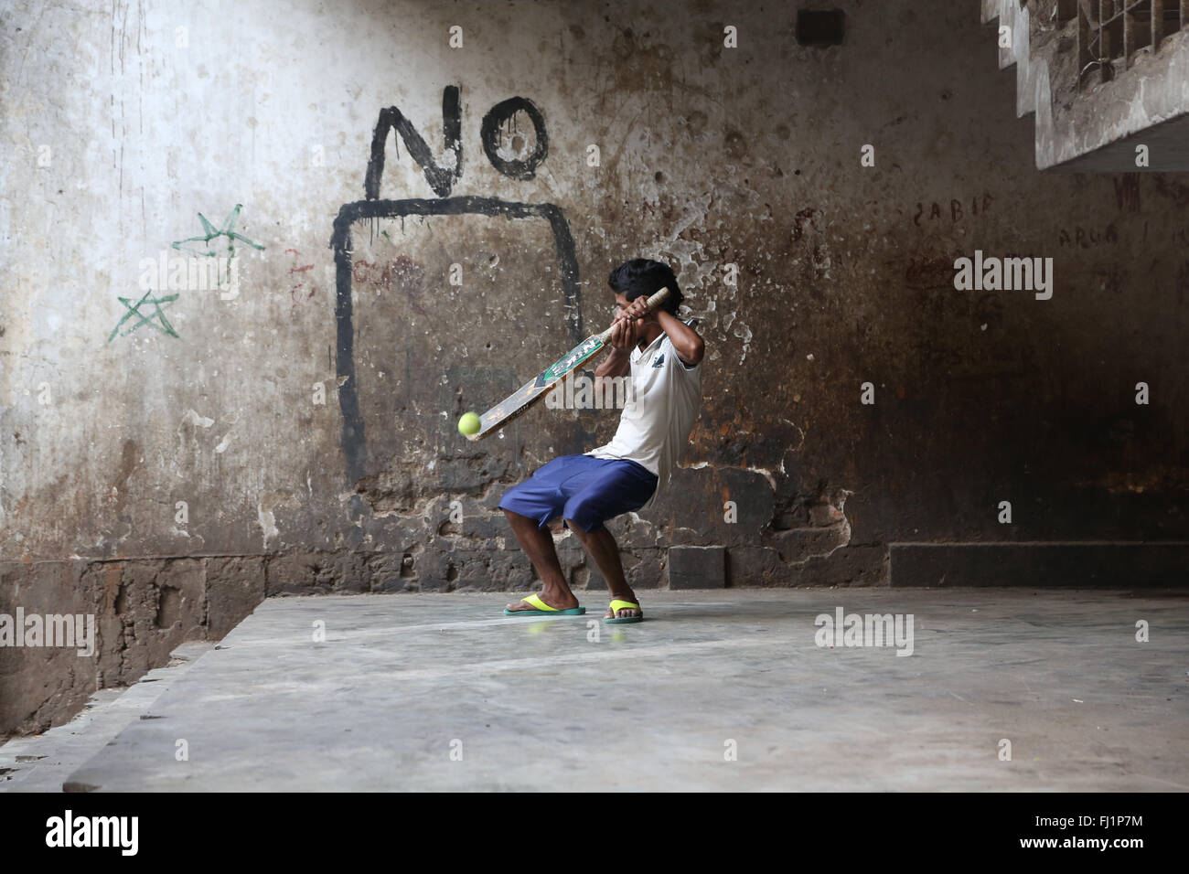 Junger Mann spielen Kricket in der Nähe von neuen Markt, Kolkata, mit einem 'Nein' Schrift an der Wand hinter ihm. Er vermisst die Kugel. Stockfoto