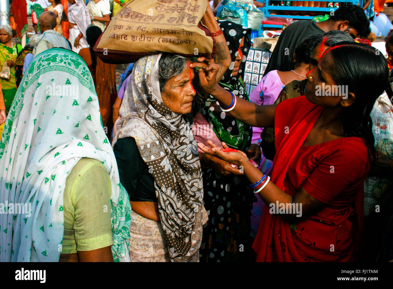 Frauen drawning tilak Segen auf der Stirn eines alten Pilger auf einer Ghat von Varanasi, Indien Stockfoto