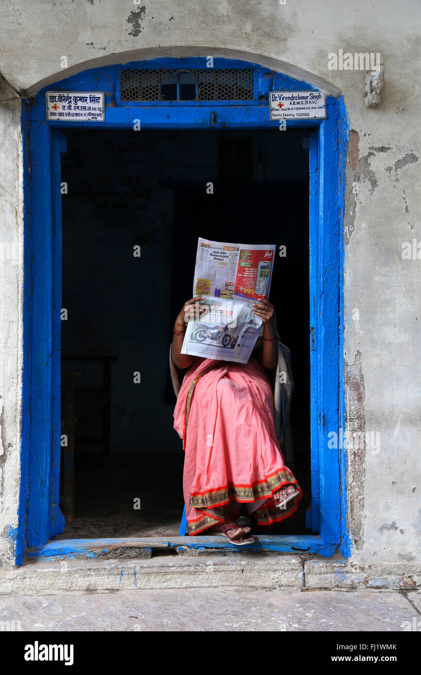 Frau liest Zeitung am Eingang ihres Hauses im Alten Stadt Varanasi, Indien Stockfoto