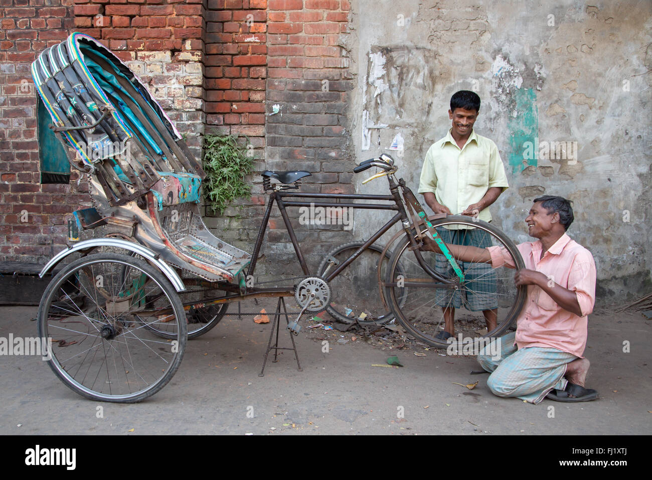 Ein lächelnder Mann Reparaturen/Änderungen eine Rikscha Reifenpanne mit glücklichen Kunden, Chittagong, Bangladesch Stockfoto