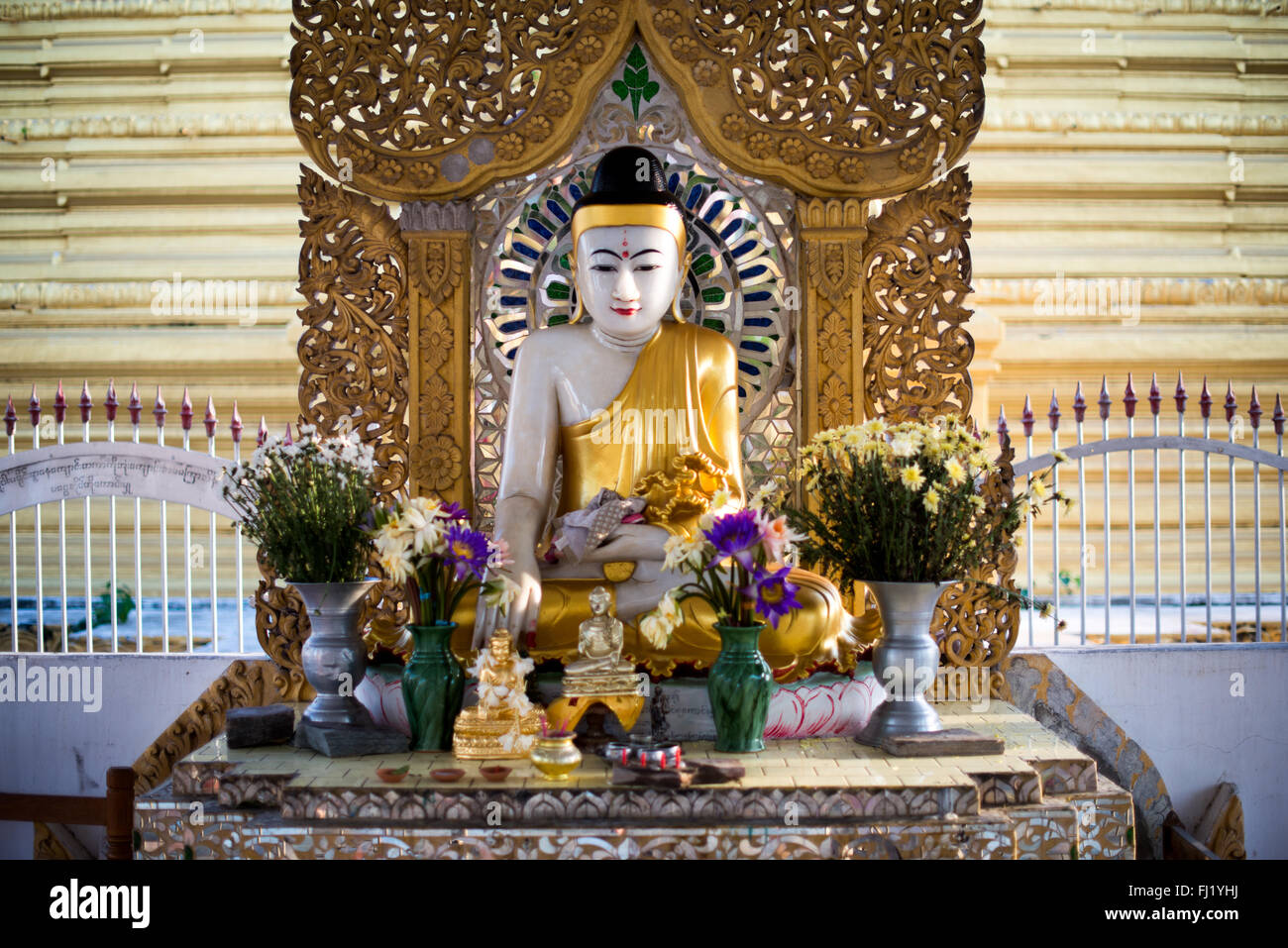 MANDALAY, Myanmar – Eine sitzende Buddha-Statue und ein kleiner Schrein auf dem Gelände der Kuthodaw-Pagode. Der Tempelkomplex, der 1857 während der Regierungszeit von König Mindon erbaut wurde, beherbergt das als das größte Buch der Welt bekannt ist. Der Schrein stellt einen von vielen Andachtsräumen innerhalb des Tempelgeländes dar. Stockfoto