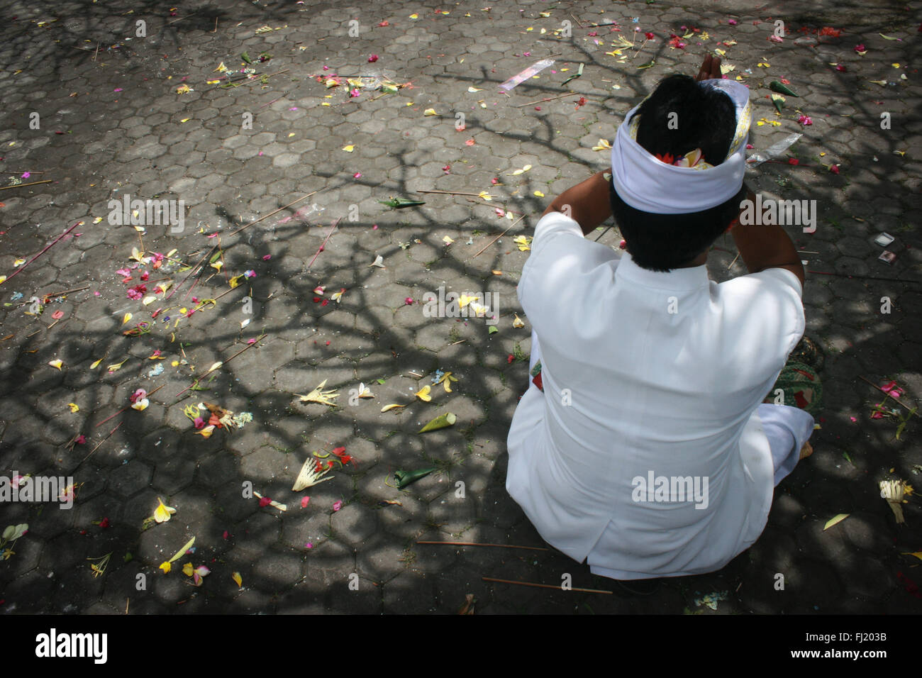 Hinduistischen Mann betend auf dem Boden mit Schatten eines Baumes und Blüten in Ubud, Indonesien Stockfoto