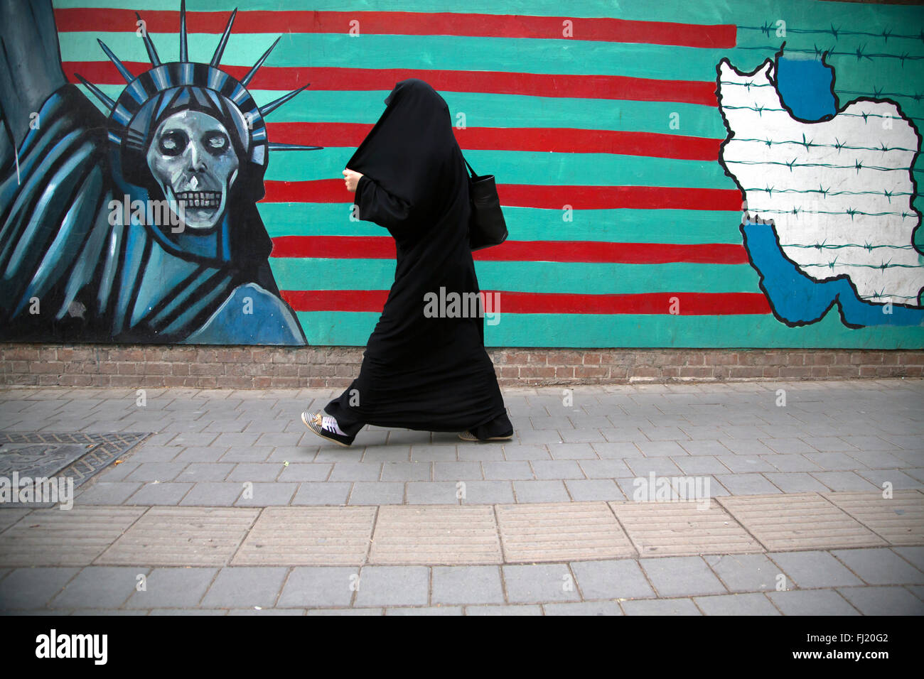 Eine Frau Spaziergänge entlang ein eindrucksvolles Wandgemälde an der Wand der ehemaligen US-Botschaft/US Höhle der Spionage in Teheran, Iran Stockfoto