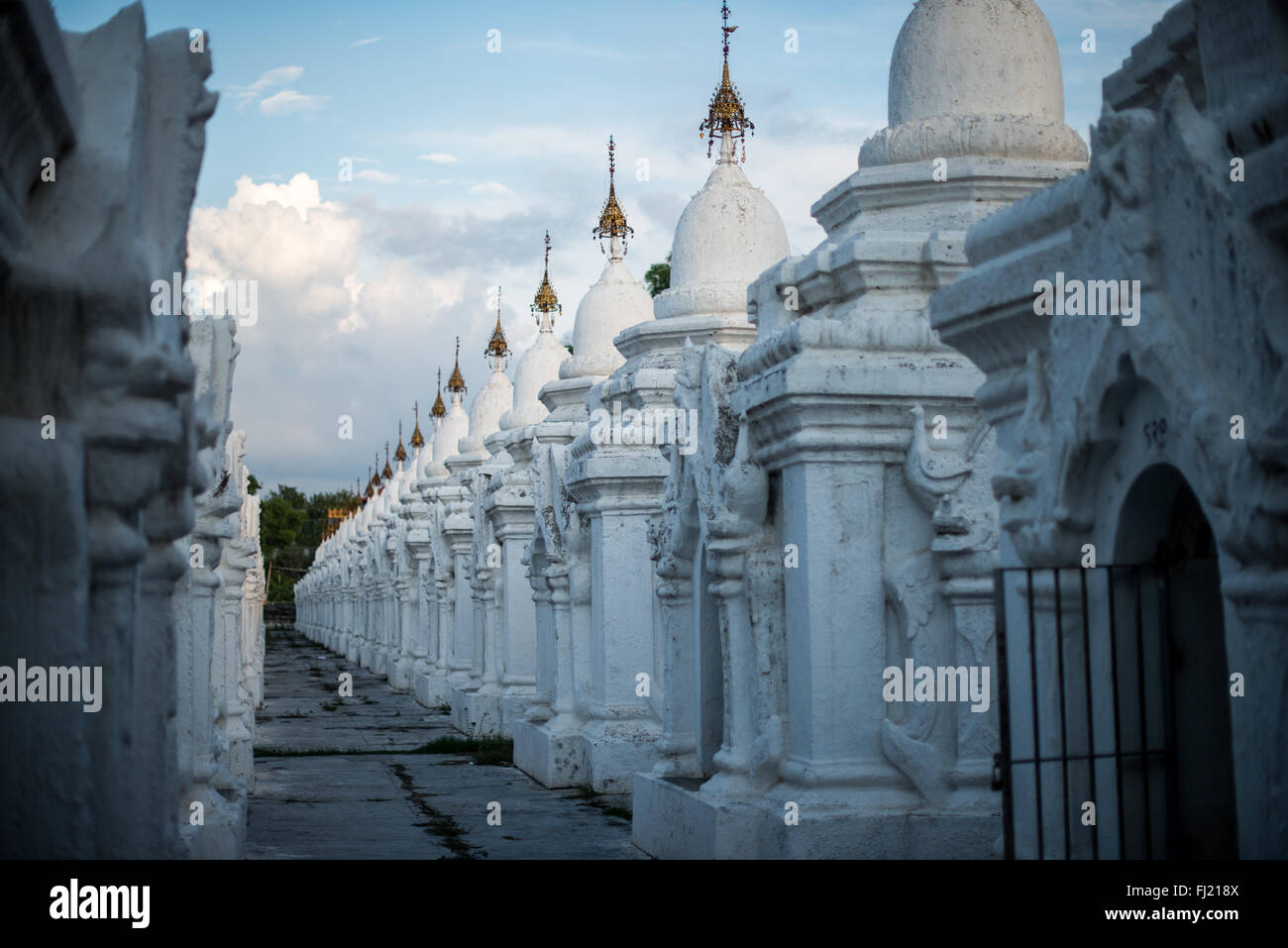 MANDALAY, Myanmar – Reihen von unberührten weißen Kyauksa gu (Höhlen mit Steininschriften) erstrecken sich über das Gelände der Kuthodaw-Pagode. Der 1857 von König Mindon erbaute Komplex enthält 729 Marmorplatten, die zusammen das als das größte Buch der Welt bekannt ist. Jede kleine Stupa beherbergt eine Marmortafel auf beiden Seiten mit Text aus dem Tipitaka, dem vollständigen Pali-Kanon des Theravada-Buddhismus. Die geordnete Anordnung dieser Strukturen spiegelt traditionelle buddhistische Architekturprinzipien wider. Stockfoto