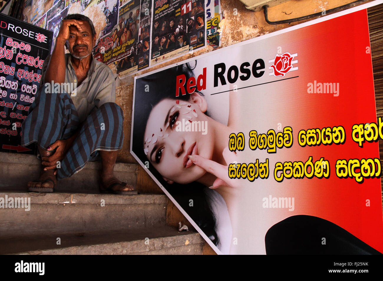 Mann sitzt alleine auf der Treppe mit Frau Poster an der Wand in Kandy, Sri Lanka Stockfoto