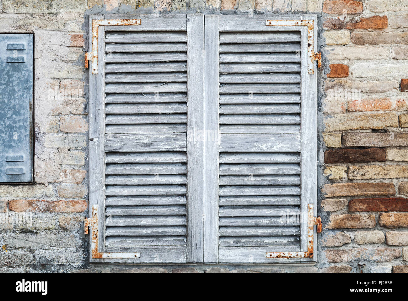 Alte Fenster mit weißen geschlossenen Fensterläden aus Holz in Ziegelmauer Hintergrundtextur Foto Stockfoto