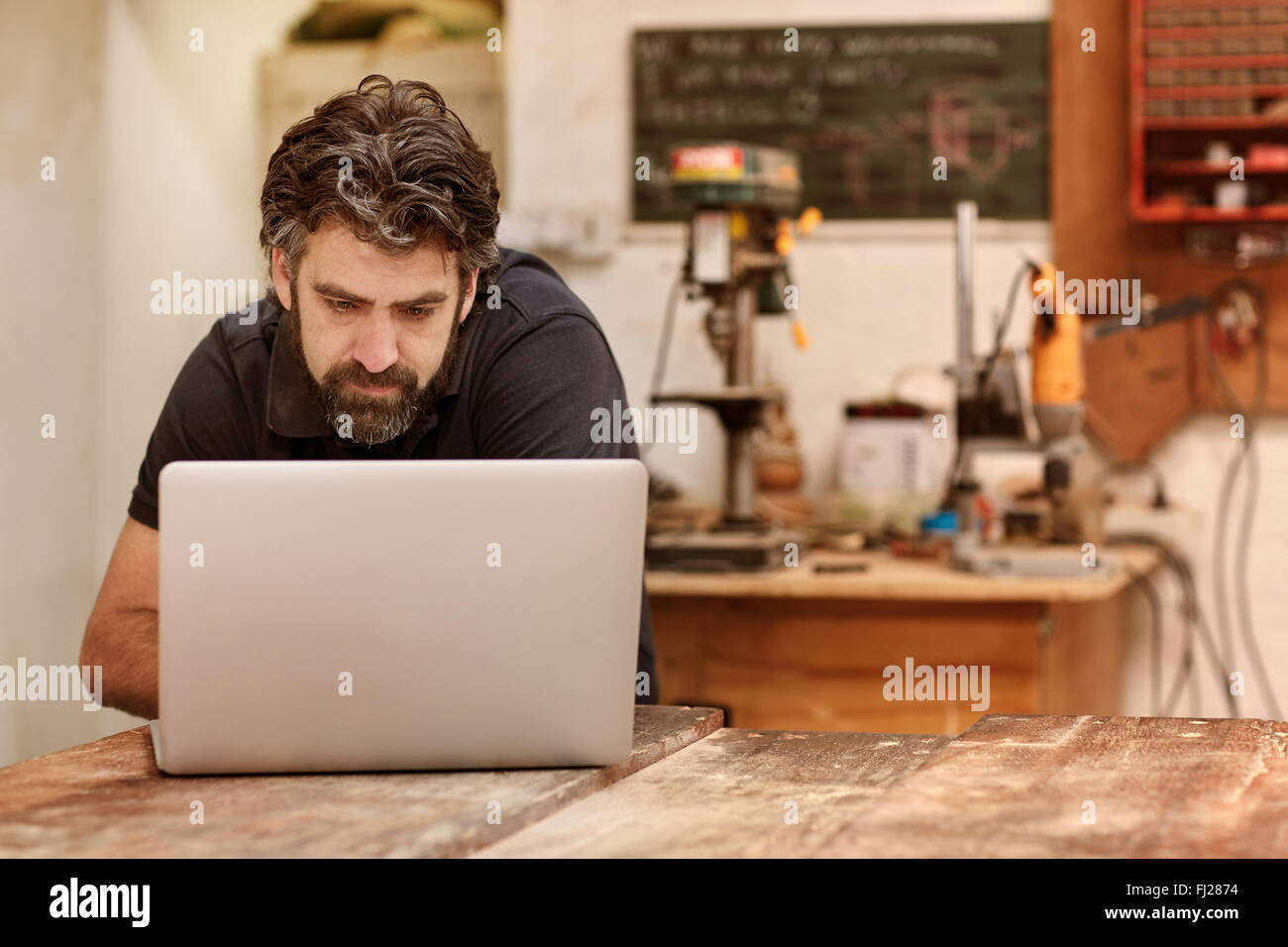 Holzarbeiten-Designer mit einem Bart in seiner Werkstatt mit laptop Stockfoto