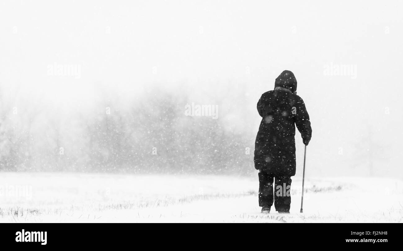 Alte Frau mit Krücke gehen in Schnee Schneesturm Stockfoto