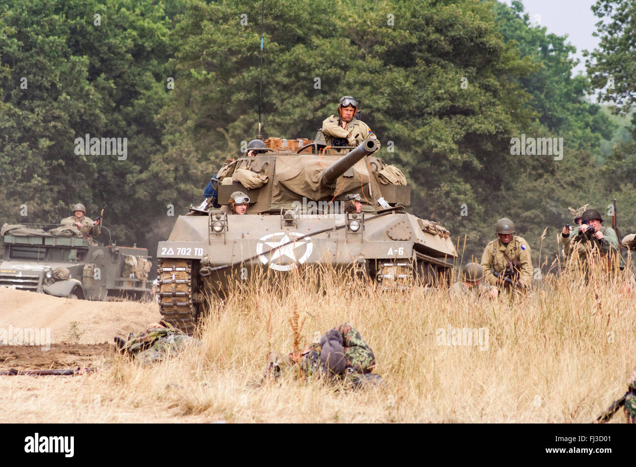 Zweiten Weltkrieg Re-enactment. Us medium Tank M18 Hellcat, mit Infanterieunterstützung, Förderung durch hohes Gras in Richtung Betrachter während der Schlacht. Stockfoto