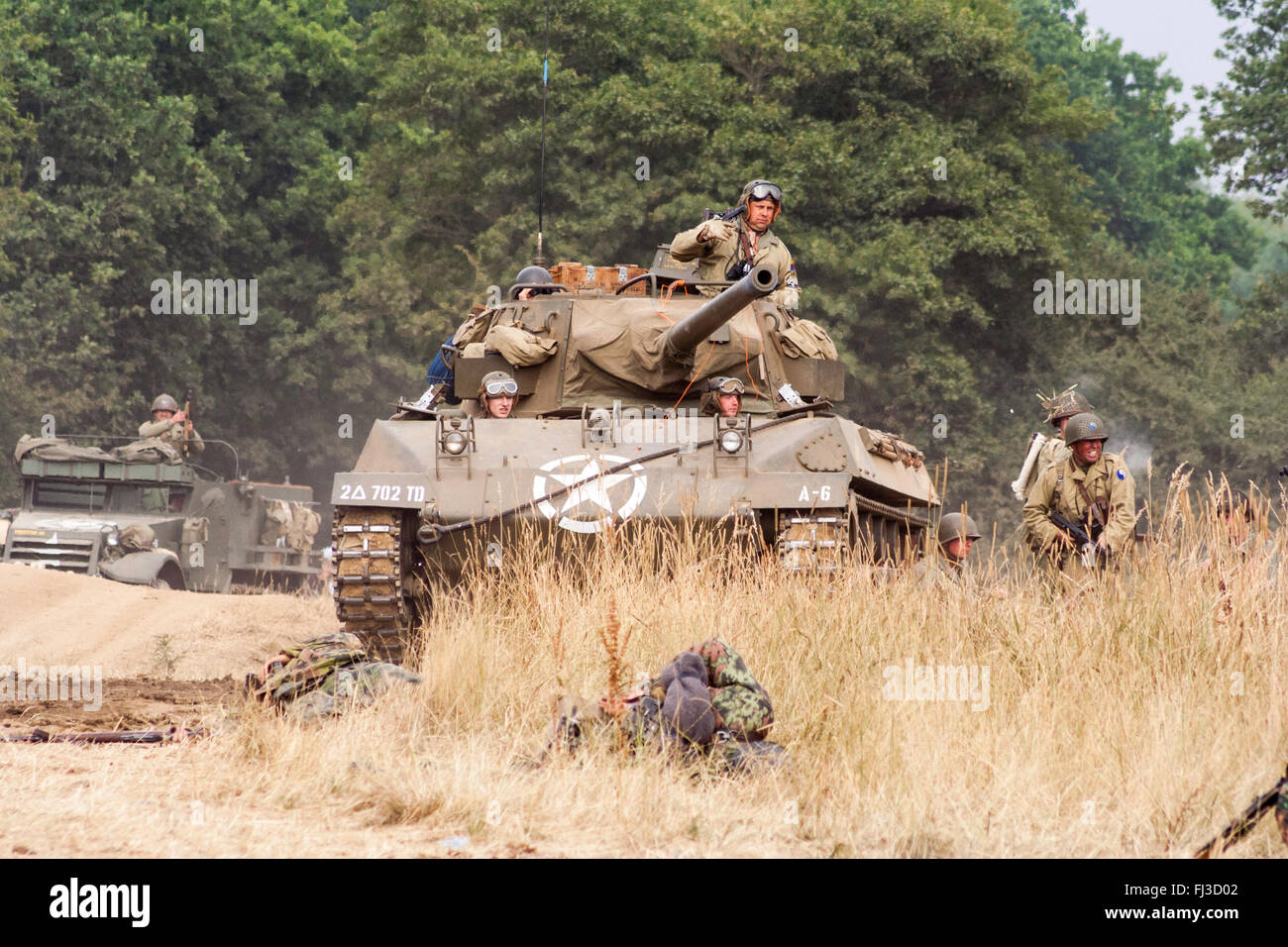 Zweiten Weltkrieg Re-enactment. Us medium Tank M18 Hellcat, mit Infanterieunterstützung, Förderung durch hohes Gras in Richtung Betrachter während der Schlacht. Stockfoto