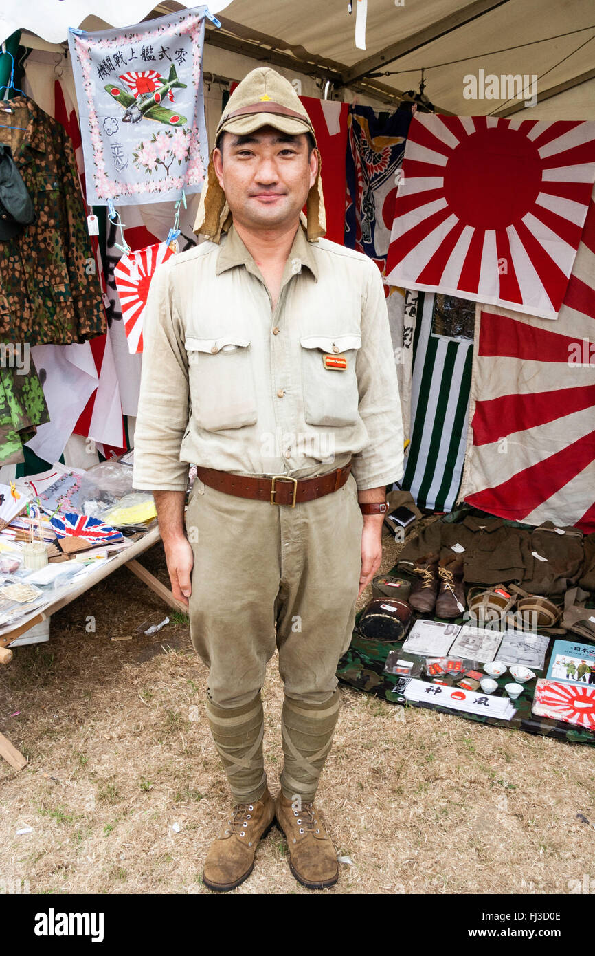 Re-enactment. Lächelnd japanischen Soldaten im Zweiten Weltkrieg uniform, ständigen Aufmerksamkeit vor Krieg Fahnen und Erinnerungsstücke. Stockfoto