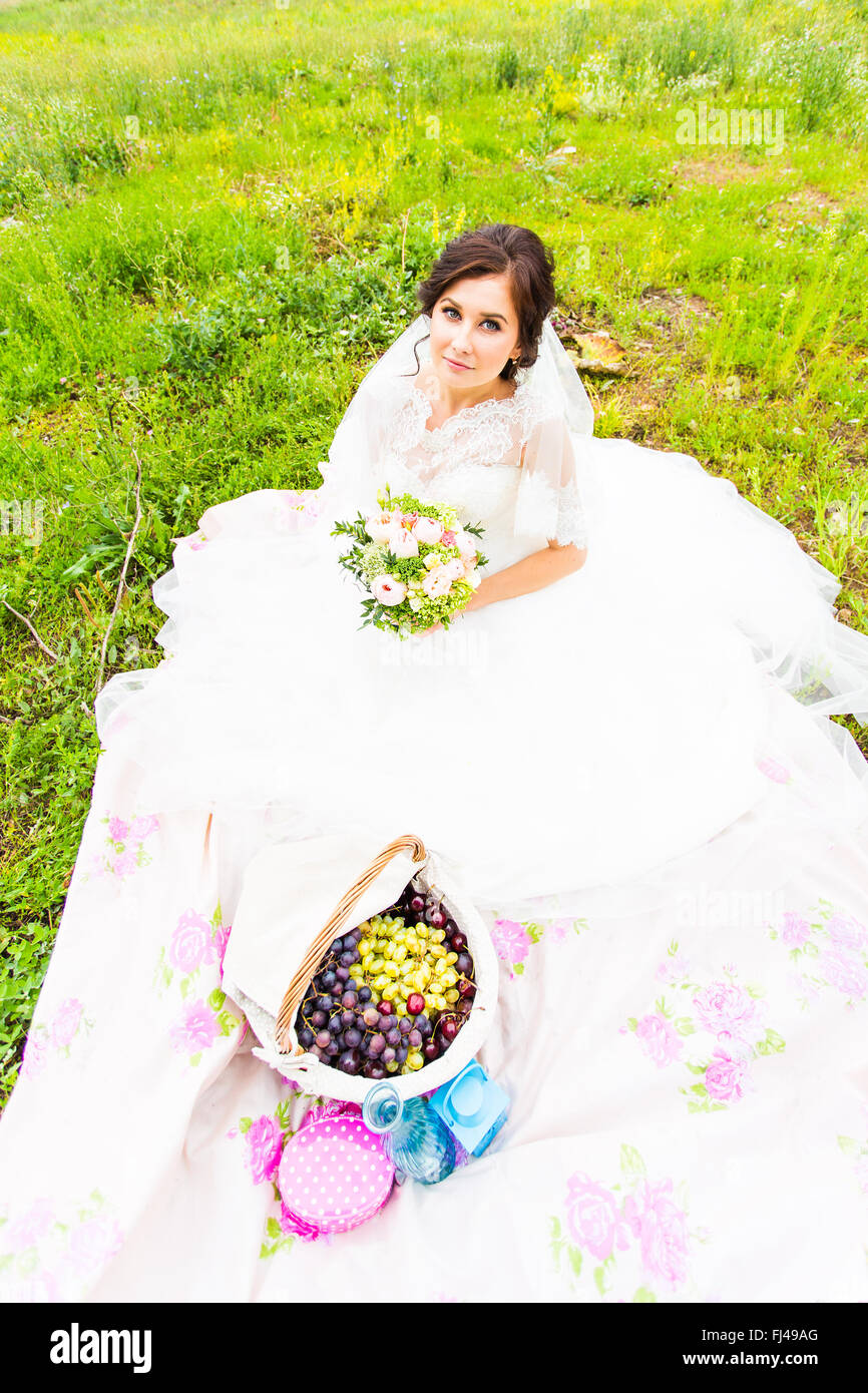 Braut sitzt auf einer Wiese mit einem großen Korb mit Früchten Stockfoto