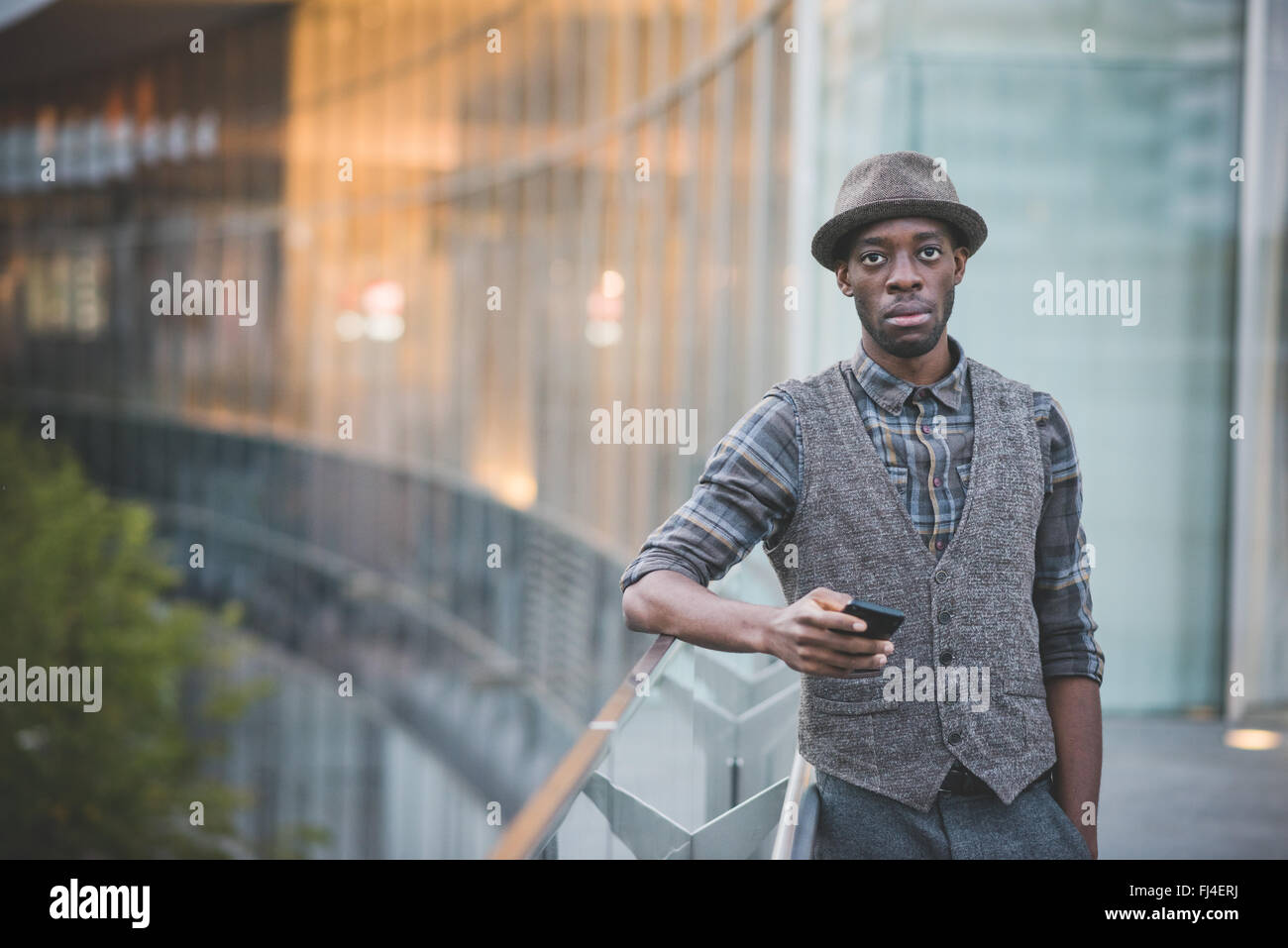 Knie-Figur des schönen jungen Afro Mann hält eine Smartphone stützte sich auf einen Handlauf auf der Suche in der Kamera Exemplar auf linken Seite - soziales Netzwerk, Kommunikation, Technologie-Konzept Stockfoto