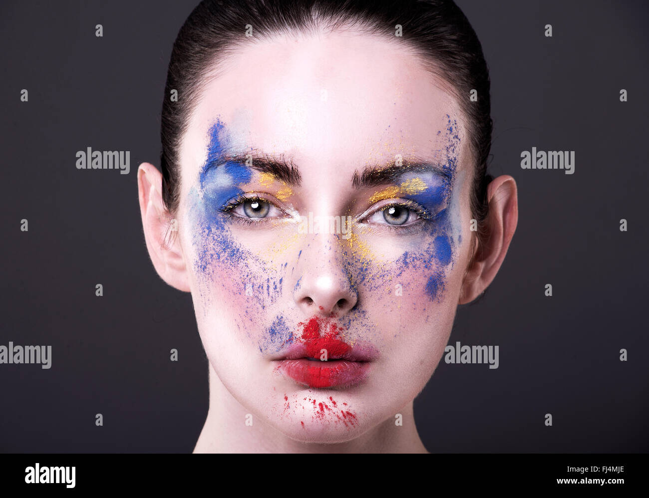 Hübsches Modell mit Puder Make-up in Primärfarben Blick direkt in die Kamera. Rot, blau und gelb Pulver auf frisches Gesicht Stockfoto