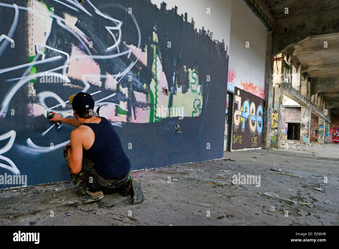 Mann sprühen Graffiti an einer Wand in eine verlassene industrielle Boden, Deutschland, Nordrhein-Westfalen, Düsseldorf Stockfoto