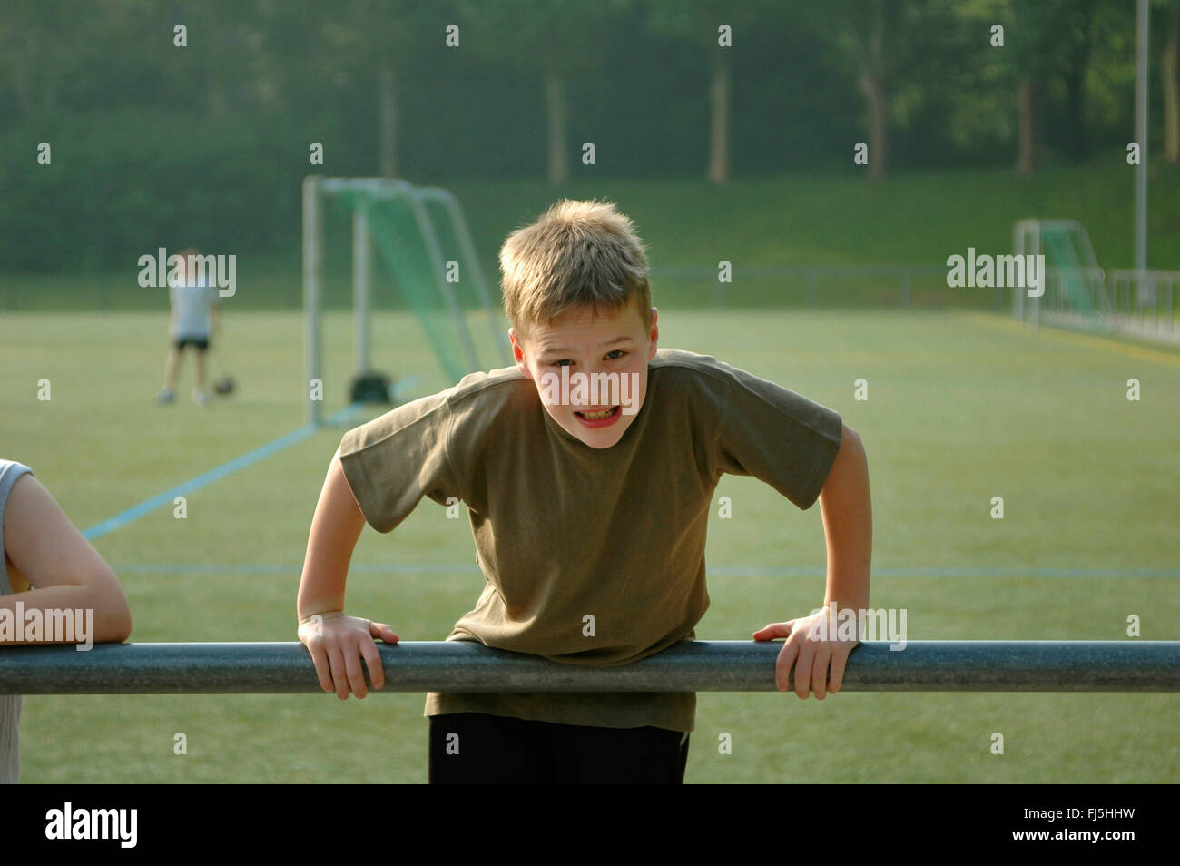 junge drücken sich über ein Geländer auf dem Fußballplatz, Porträt eines Kindes Stockfoto
