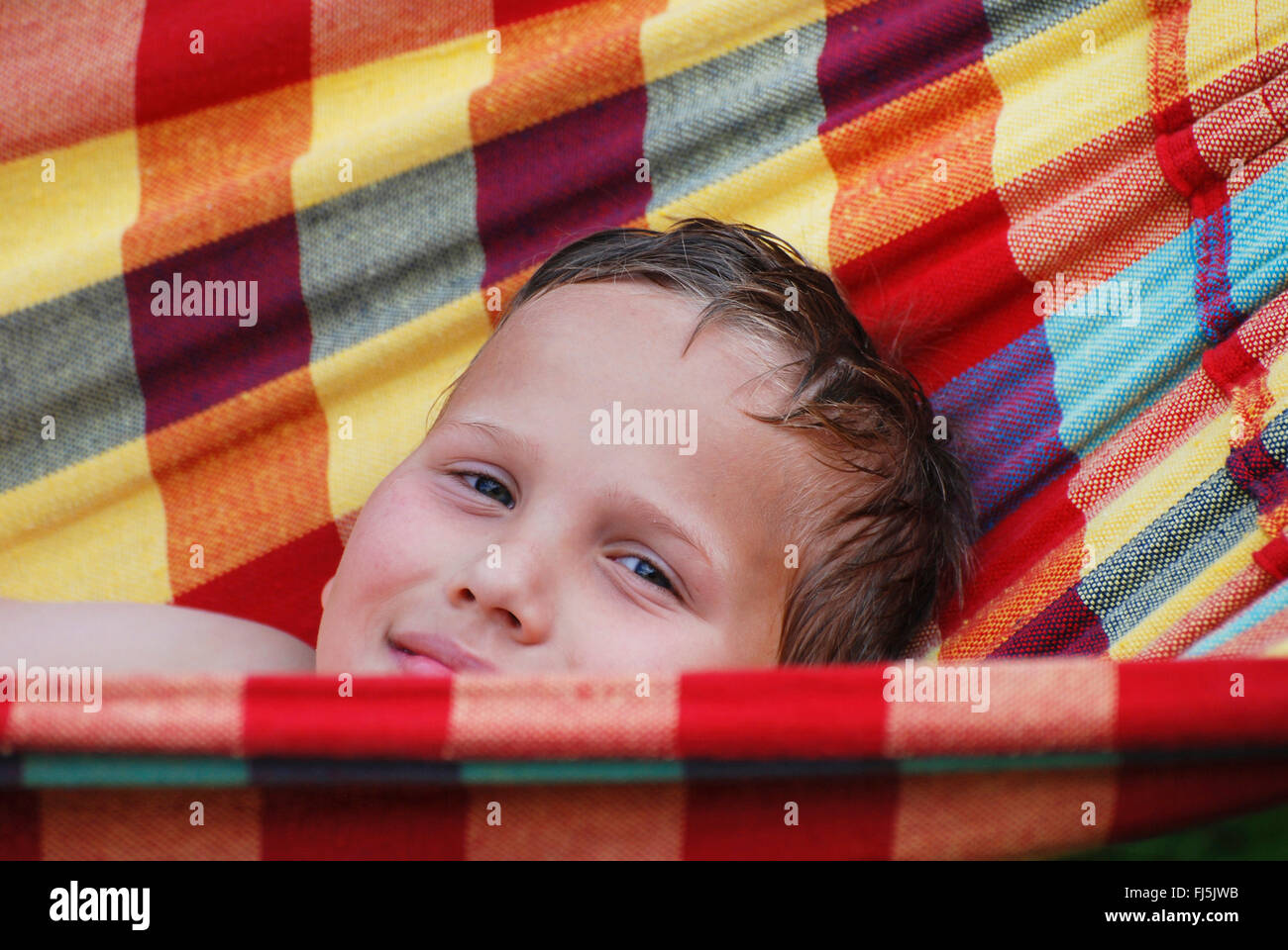 kleiner Junge liegend mit nassen Haaren in einer bunten Hängematte, Porträt eines Kindes, Deutschland Stockfoto