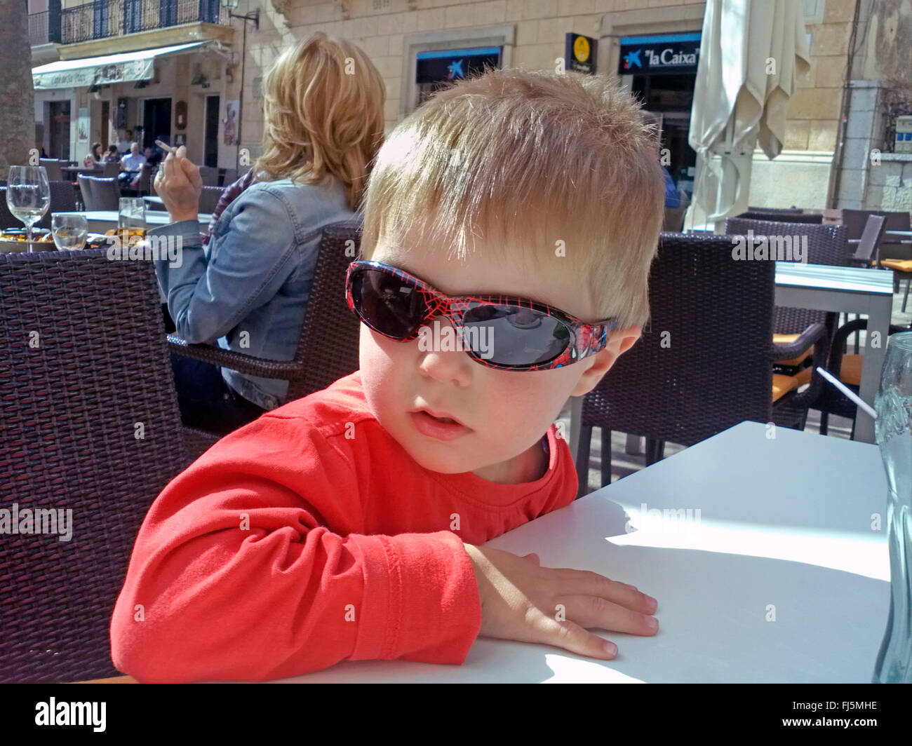 kleiner Junge mit Sonnenbrille in einem Straßencafé sitzen Stockfoto