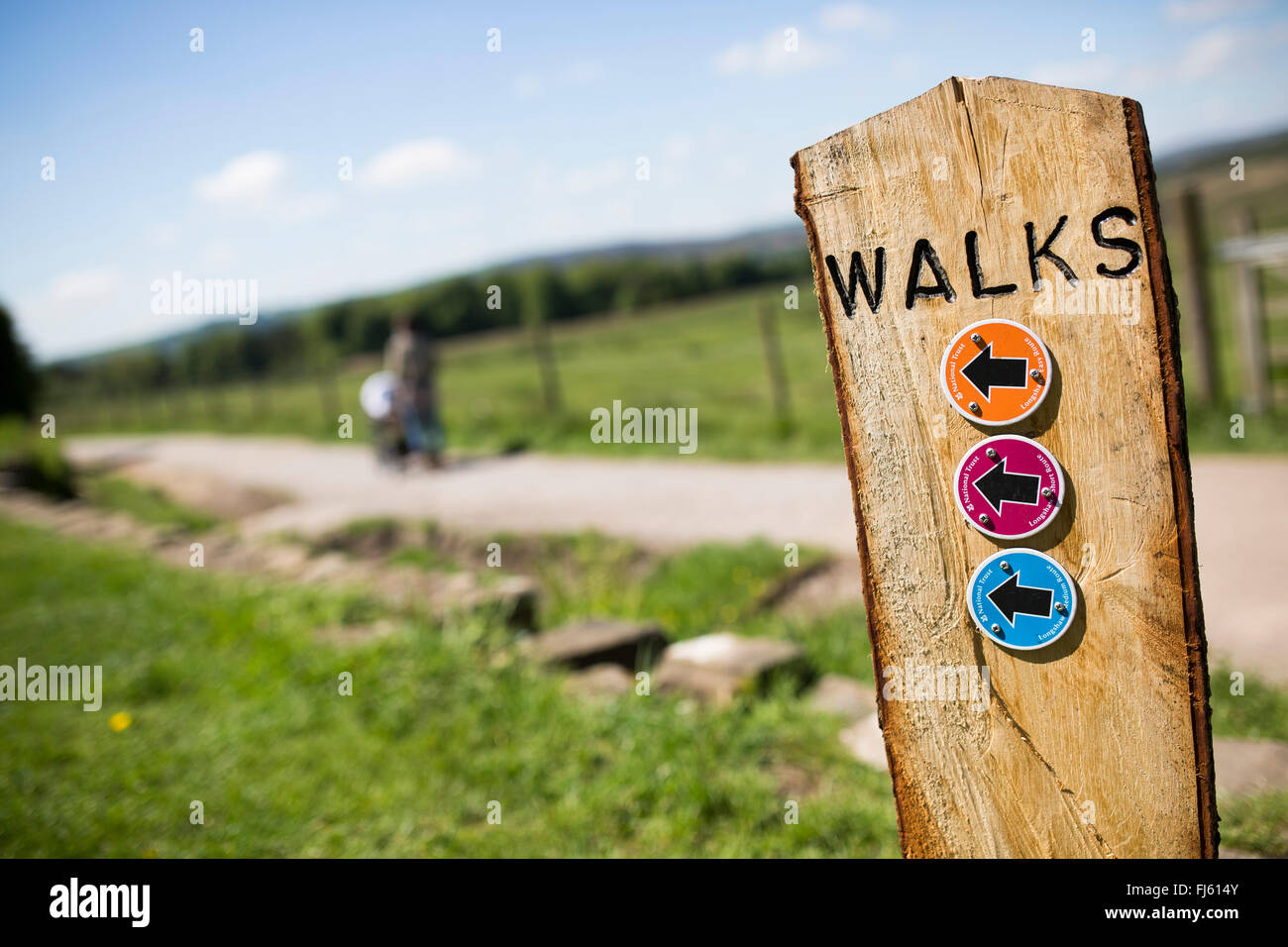 Eine Frau kommt an einem sonnigen Tag Vergangenheit ein Holzschild für Spaziergänge im Peak District. Stockfoto