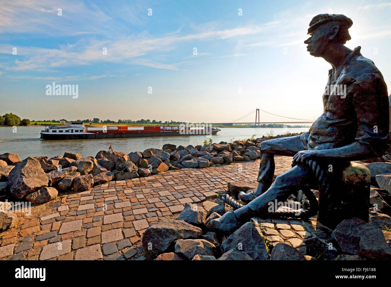 Poortekerl sitzen an der Promenade mit Blick auf den Rhein mit Frachtschiff und Rheinbrücke, Deutschland, Nordrhein-Westfalen, Niederrhein, Emmerich Stockfoto