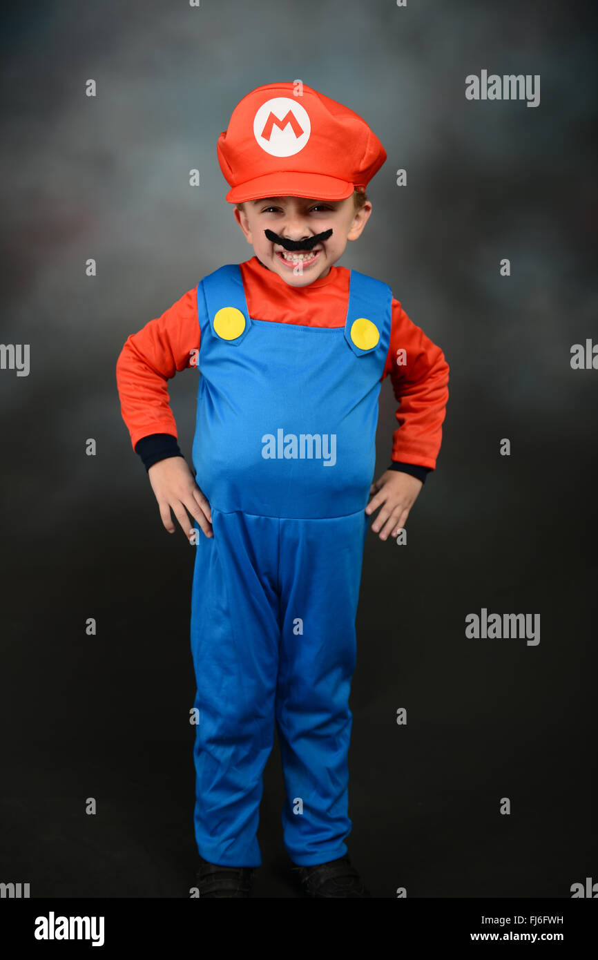 Junge verkleidete sich als Super Mario Bros vor grauem Hintergrund. Stockfoto