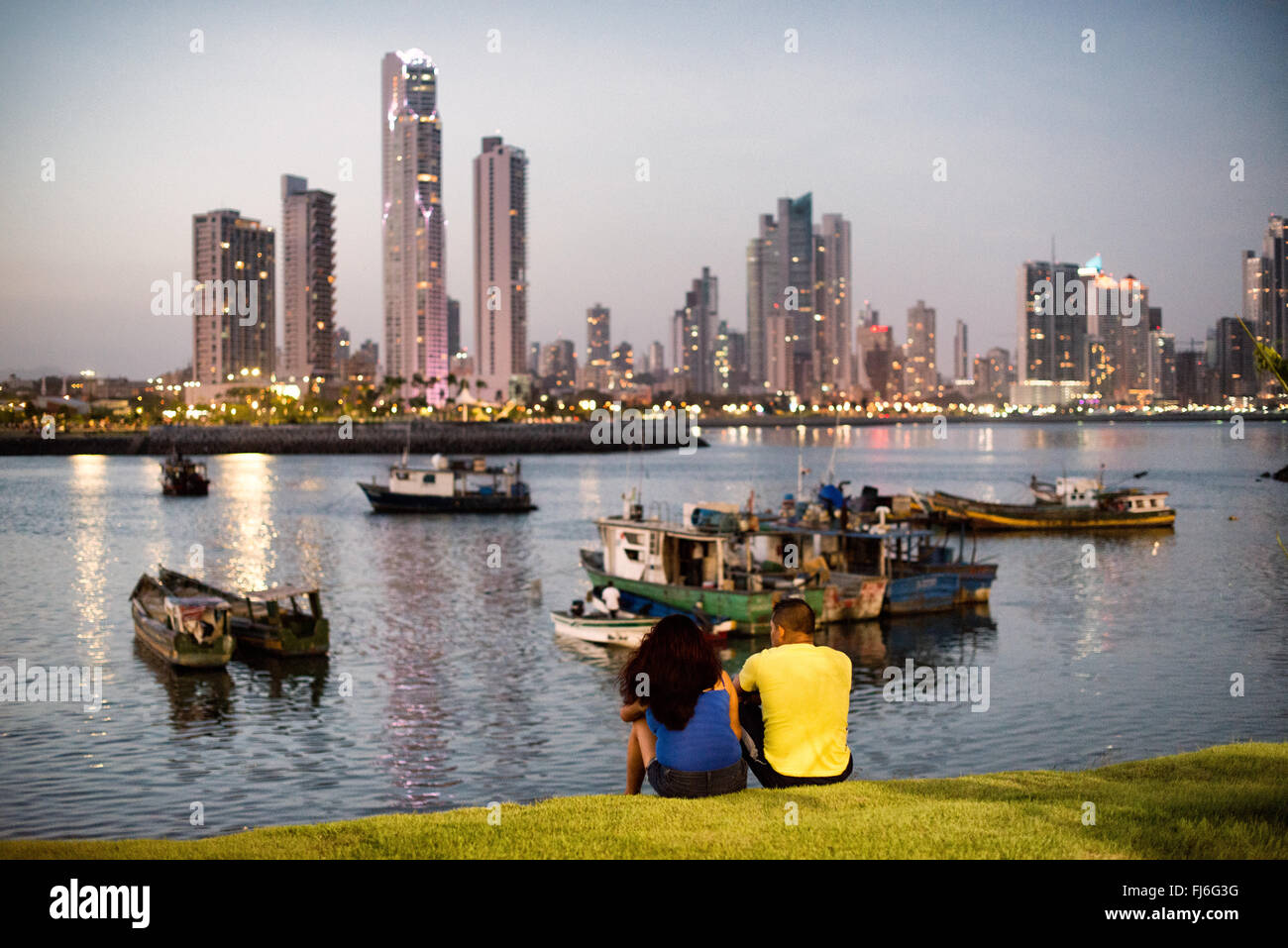 Panama-Stadt Panama // PANAMA-STADT, PANAMA — Ein Paar genießt die Aussicht an einem Sommerabend in Panama-Stadt, Panama, mit den modernen Wolkenkratzern von Punta Paitilla, die im Hintergrund ein Stadtbild bilden, mit den traditionellen Holzfischbooten von Panama-Stadt im Vordergrund. Am Ufer von Panama City, Panama, an der Panama Bay. Stockfoto