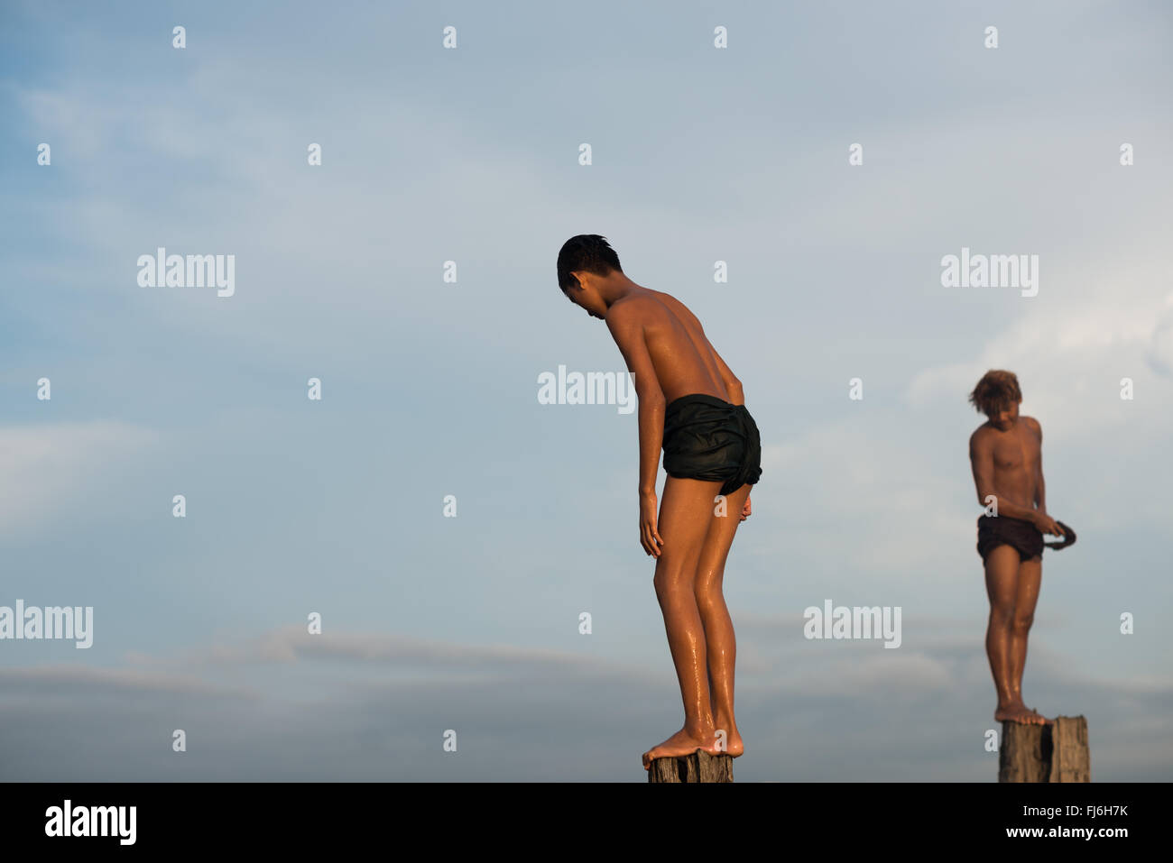 AMARAPURA, Myanmar – die U Bein Bridge erstreckt sich über den Taungthaman Lake bei Mandalay. Die 1,2 Kilometer lange Teakholzkonstruktion, die vermutlich die älteste und längste Teakholzbrücke der Welt ist, ist vom Himmel her umrahmt. Einheimische Fußgänger und Mönche überqueren die Brücke, während Touristen die berühmte Szene beobachten, die besonders bei Sonnenuntergang beliebt ist. Stockfoto