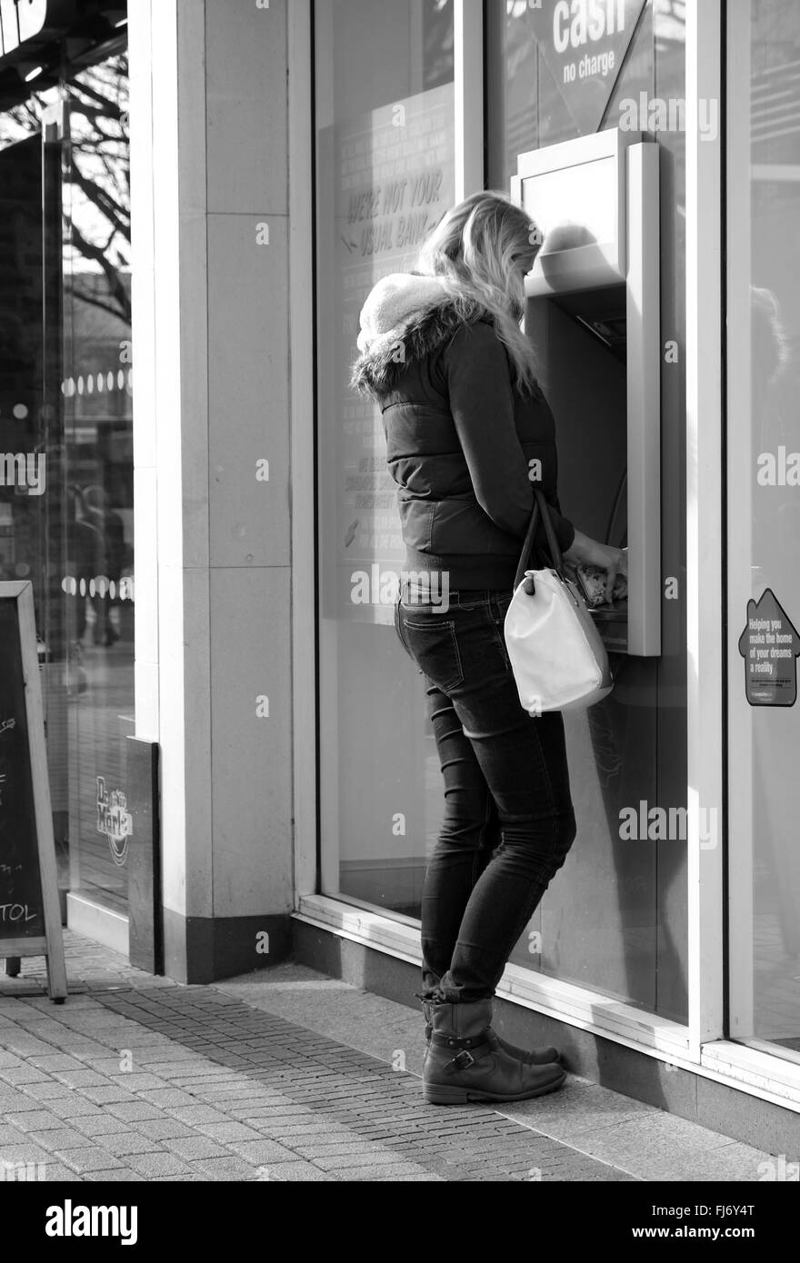 Junge Frau mit einem Loch in der Wand Punkt Geldautomat, März 2016 Stockfoto