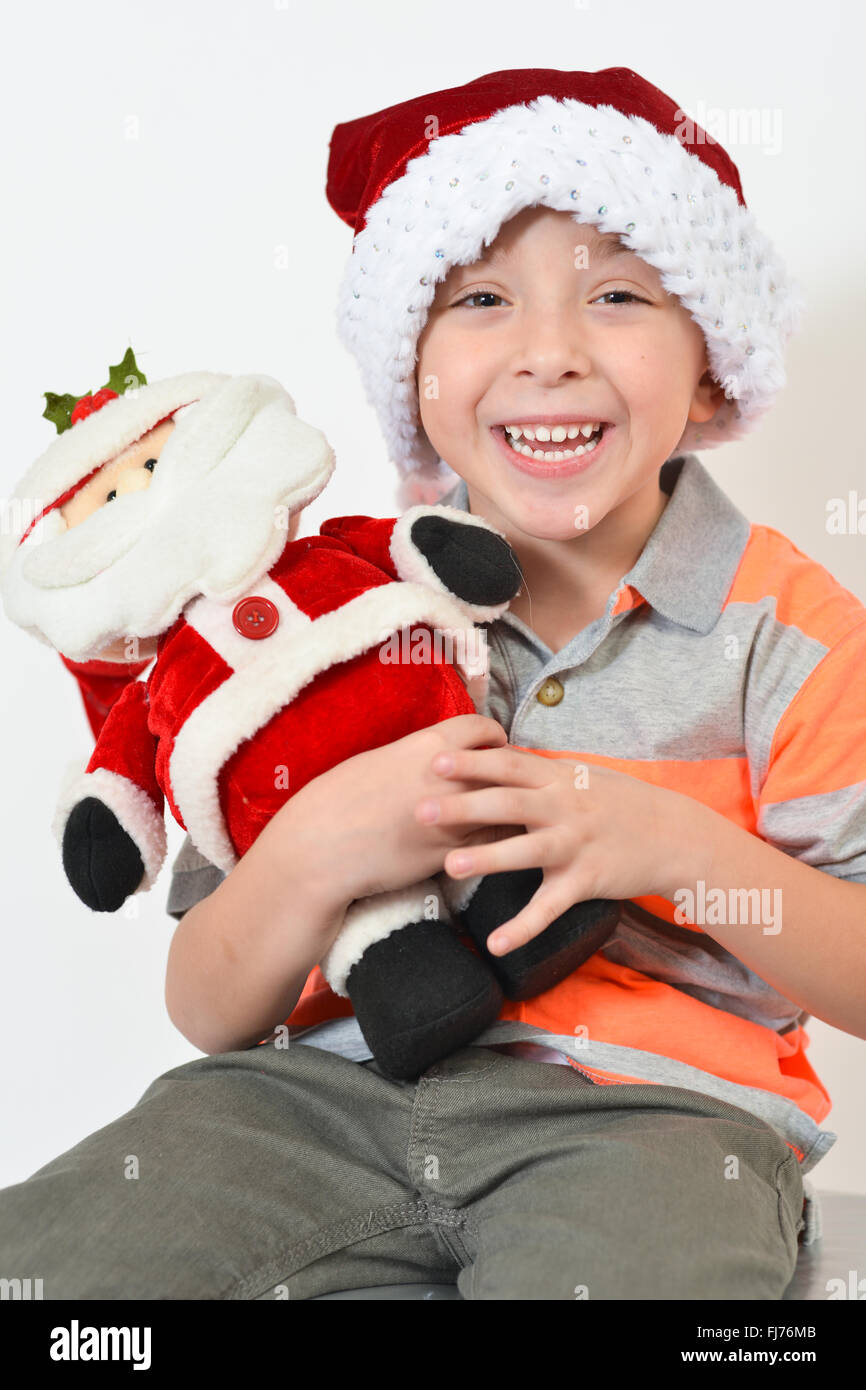 Entzückende junge hält eine Weihnachtsmann Spielzeug während des Tragens einer Weihnachtsmütze - vor weißem Hintergrund. Stockfoto