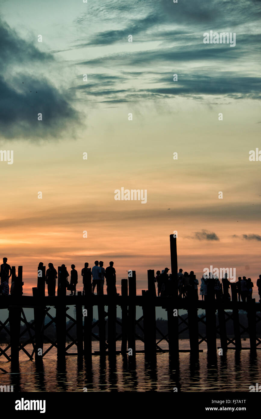 AMARAPURA, Myanmar – die U Bein Bridge erstreckt sich über den Taungthaman Lake bei Mandalay. Die 1,2 Kilometer lange Teakholzkonstruktion, die vermutlich die älteste und längste Teakholzbrücke der Welt ist, ist vom Himmel her umrahmt. Einheimische Fußgänger und Mönche überqueren die Brücke, während Touristen die berühmte Szene beobachten, die besonders bei Sonnenuntergang beliebt ist. Stockfoto