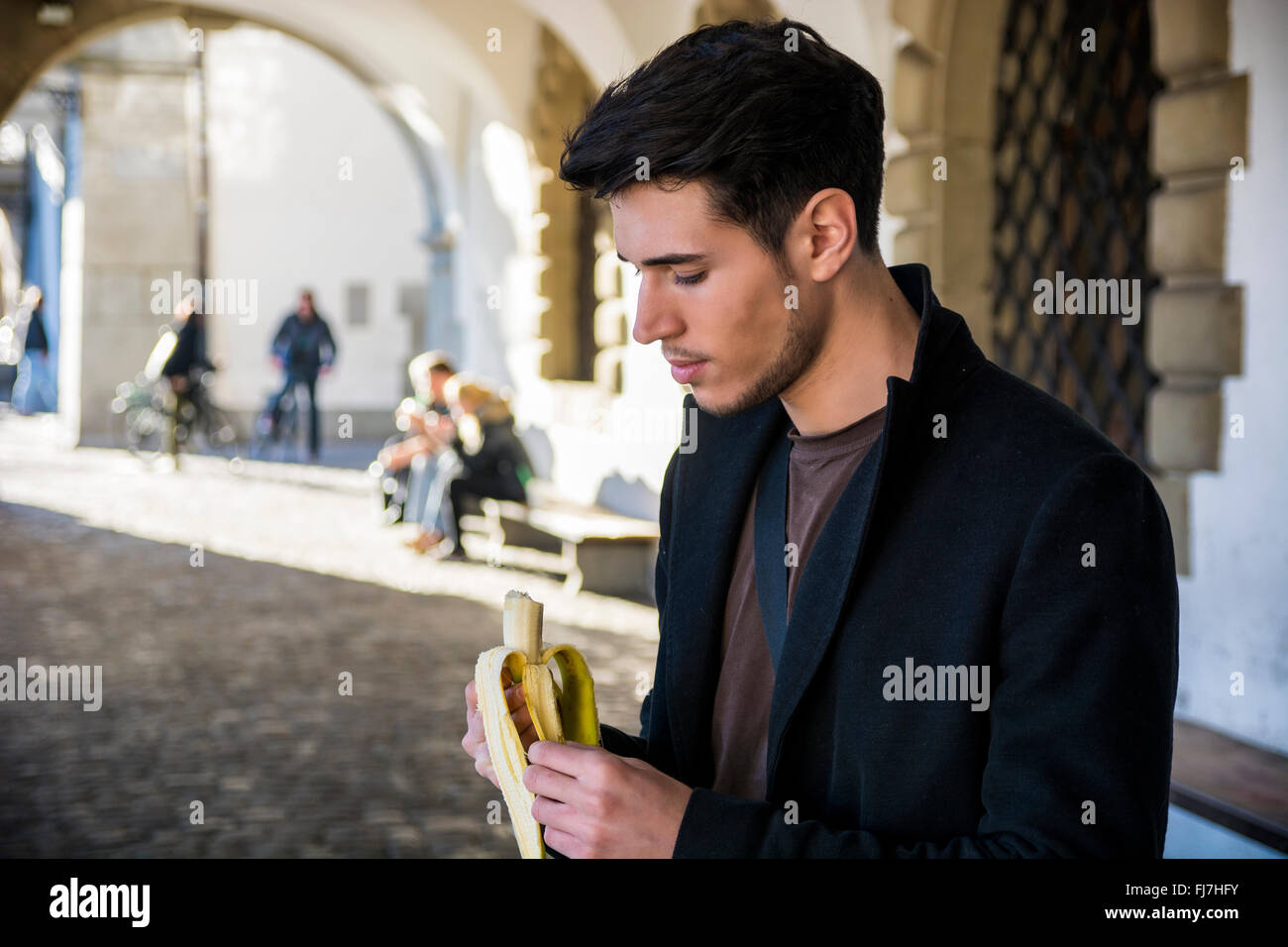 Junger Mann mit Banane auf Straße in Lausanne während der Suche nach unten stehen. Bogen Sie im Sonnenlicht auf Hintergrund Stockfoto