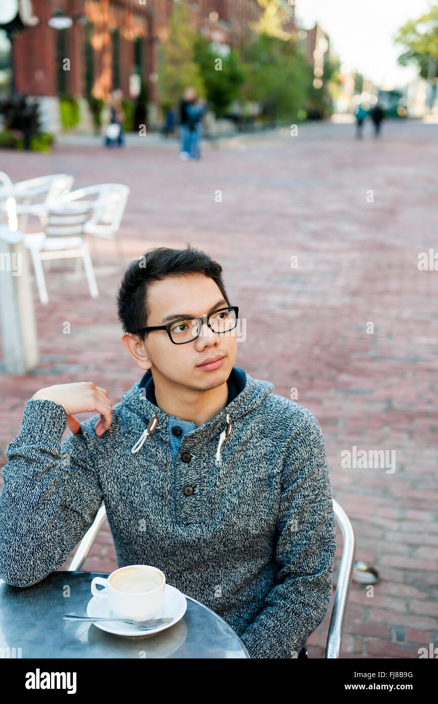Junge asiatische Mann im Straßencafé mit Tasse Kaffee mit Blick weg ernst und nachdenklich Stockfoto