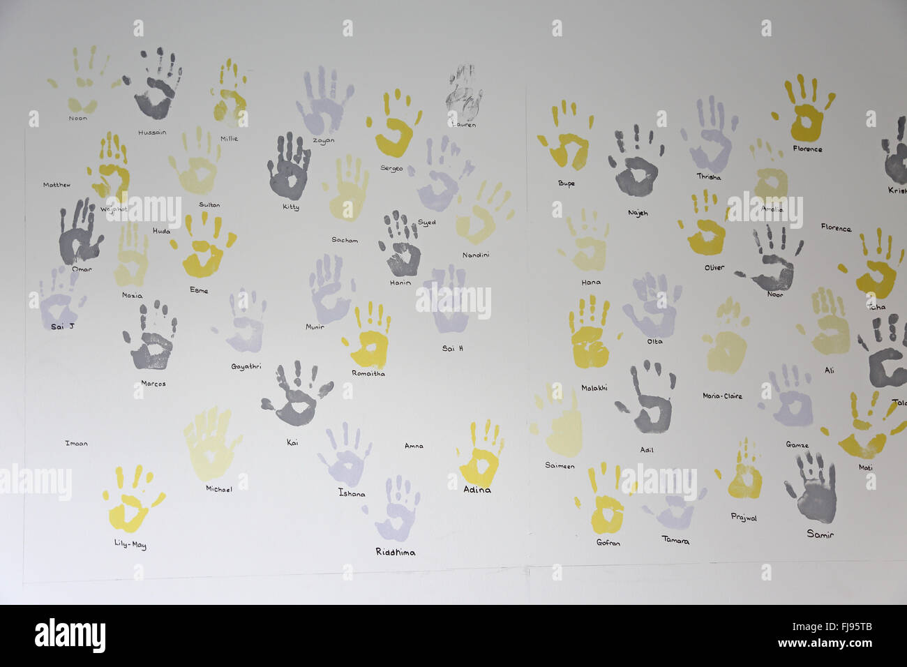 Kinder Palm druckt in grauen und gelben Farbe an der Wand einer neuen Schule. Namen sind unter jeder Druck geschrieben. Stockfoto